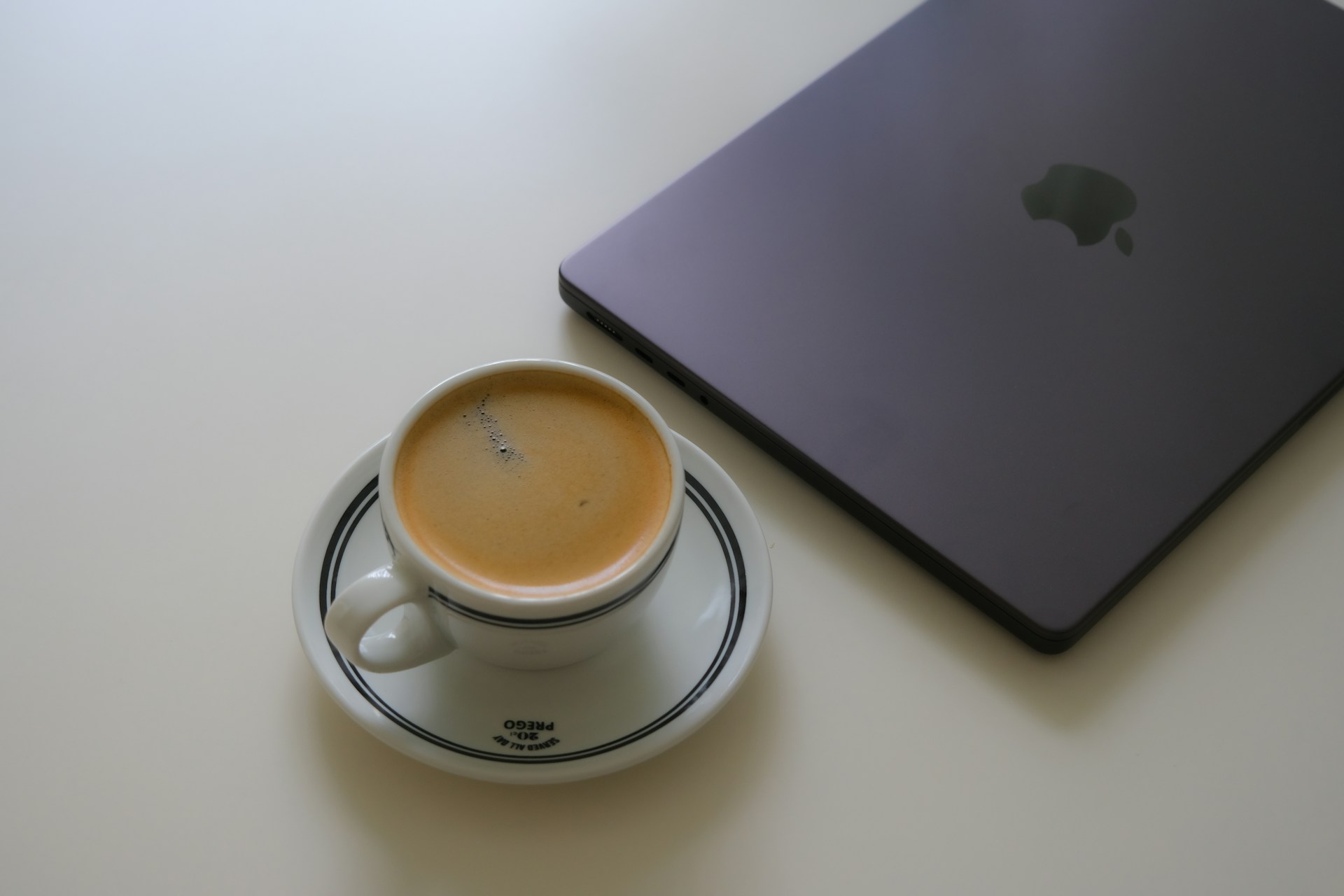 Espresso cup next to a closed laptop on white table