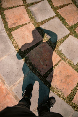 Shadow of a person standing on patterned ground.