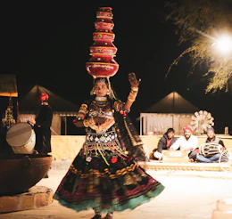 Woman balances pots on head while dancing at night.
