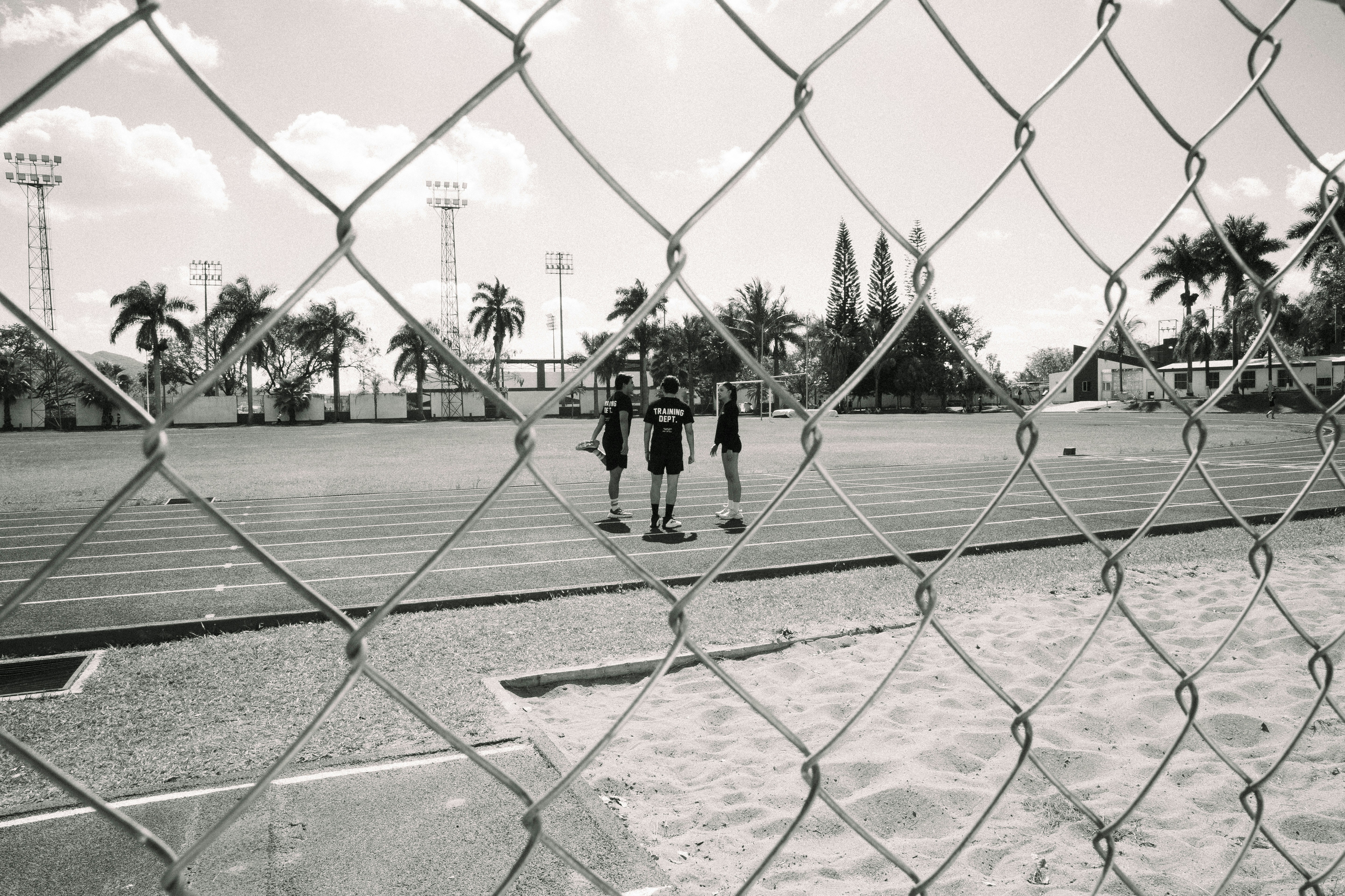 Three figures standing on a running track behind a fence