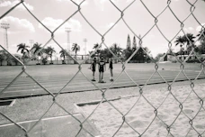 Three figures stand on a running track behind a fence.