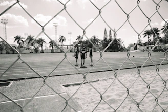 Three figures stand on a running track behind a fence.