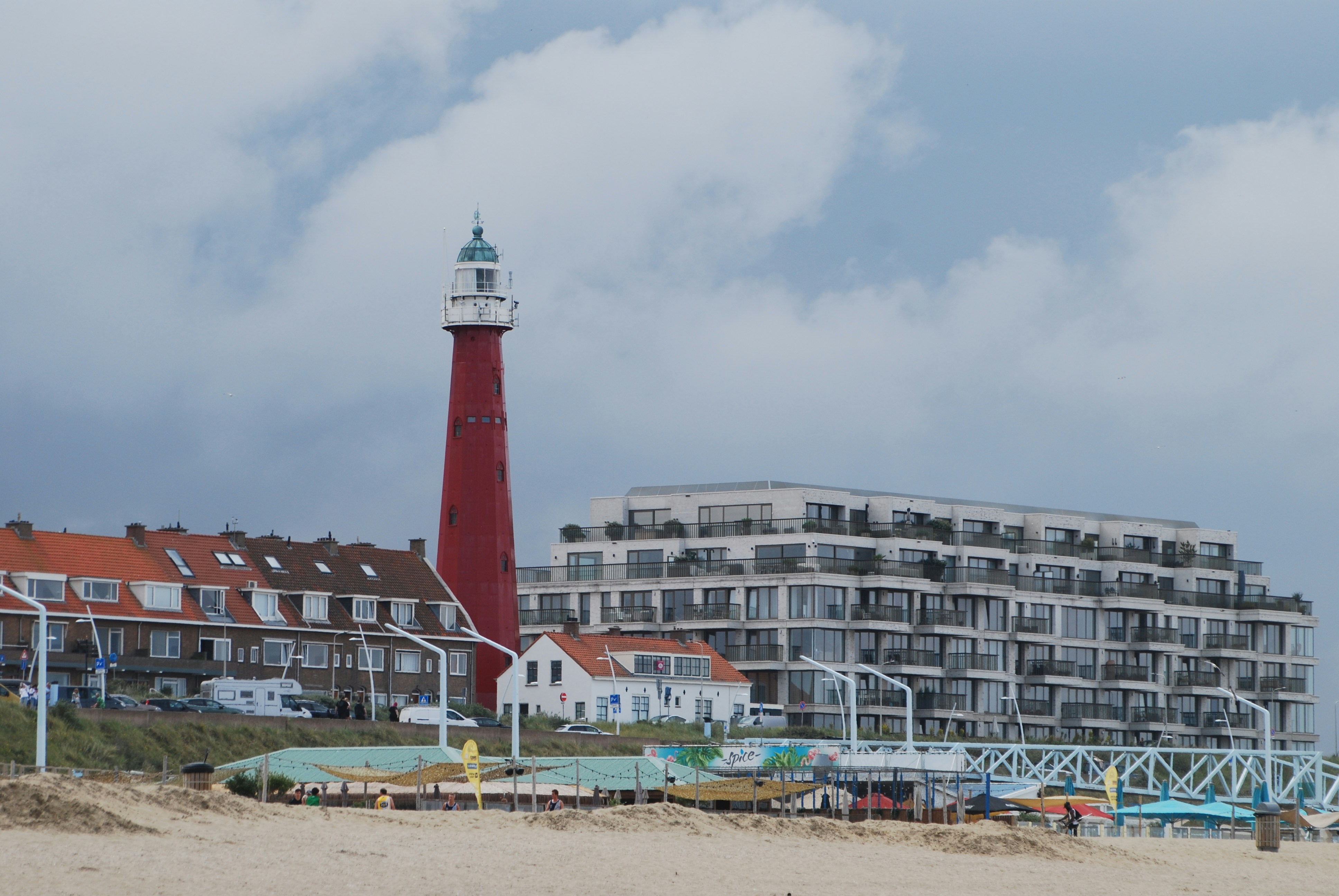 Faro rosso con edifici su una spiaggia sabbiosa.
