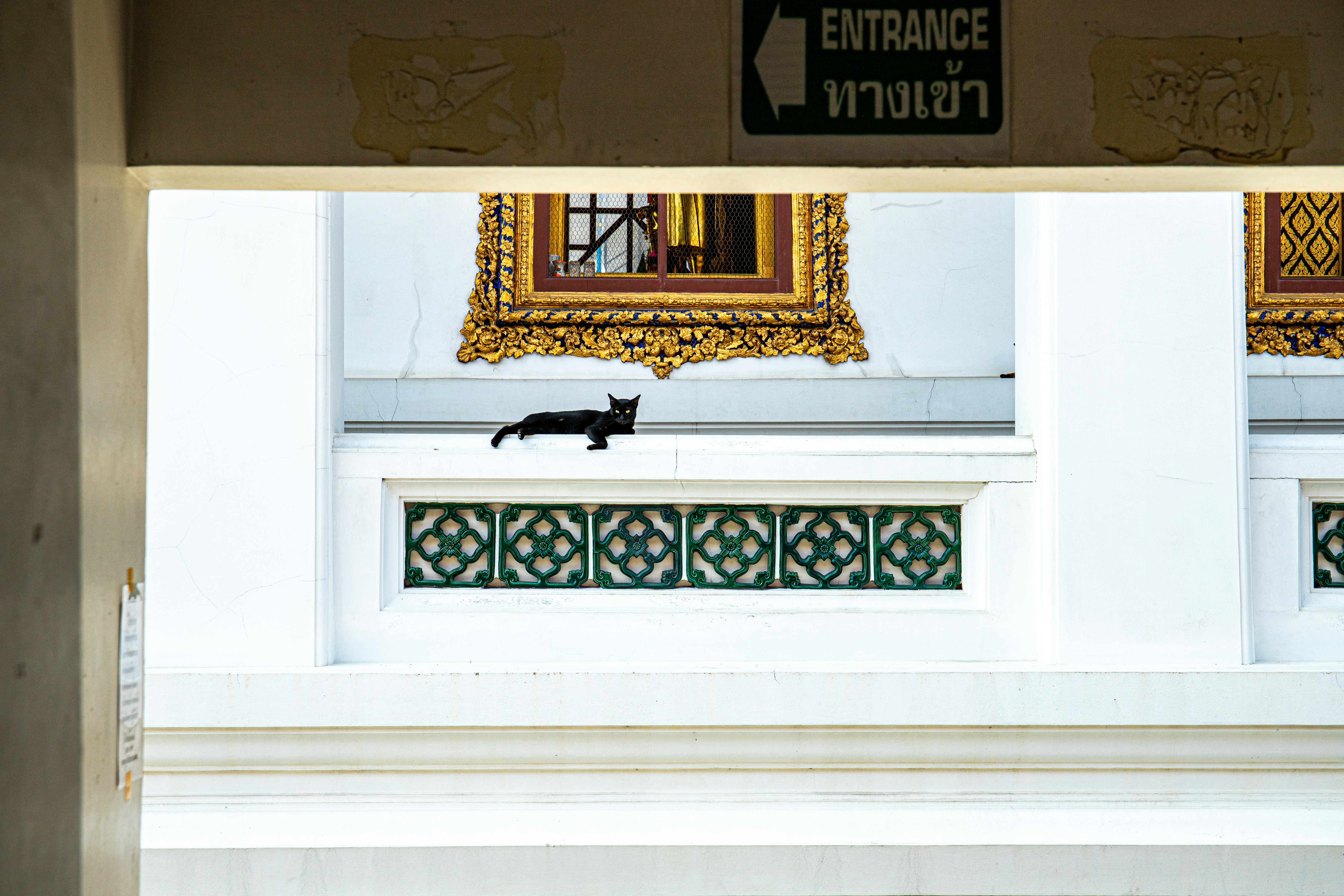 A black cat walks on a white ledge.