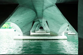 Underneath a modern concrete bridge with water below.
