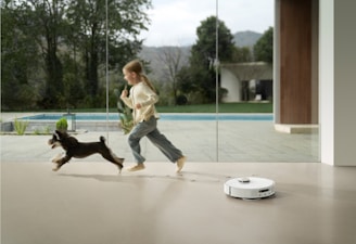 Girl and dog run past robot vacuum cleaner