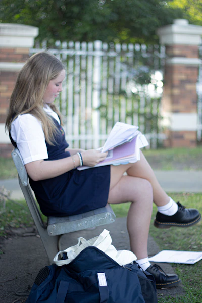 A young student reads a book on a park bench.