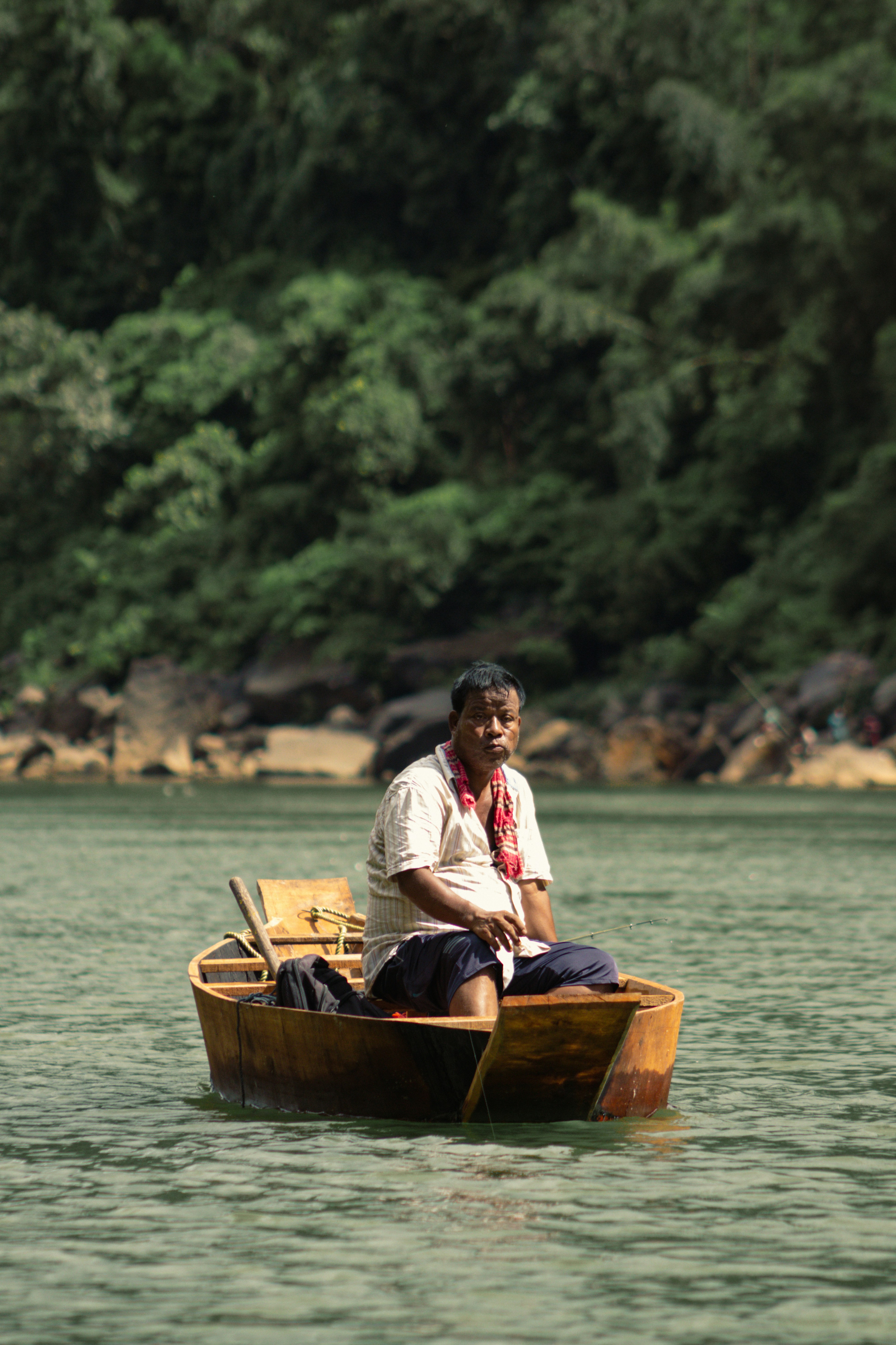 A man fishing from a small wooden boat on a river near a forest