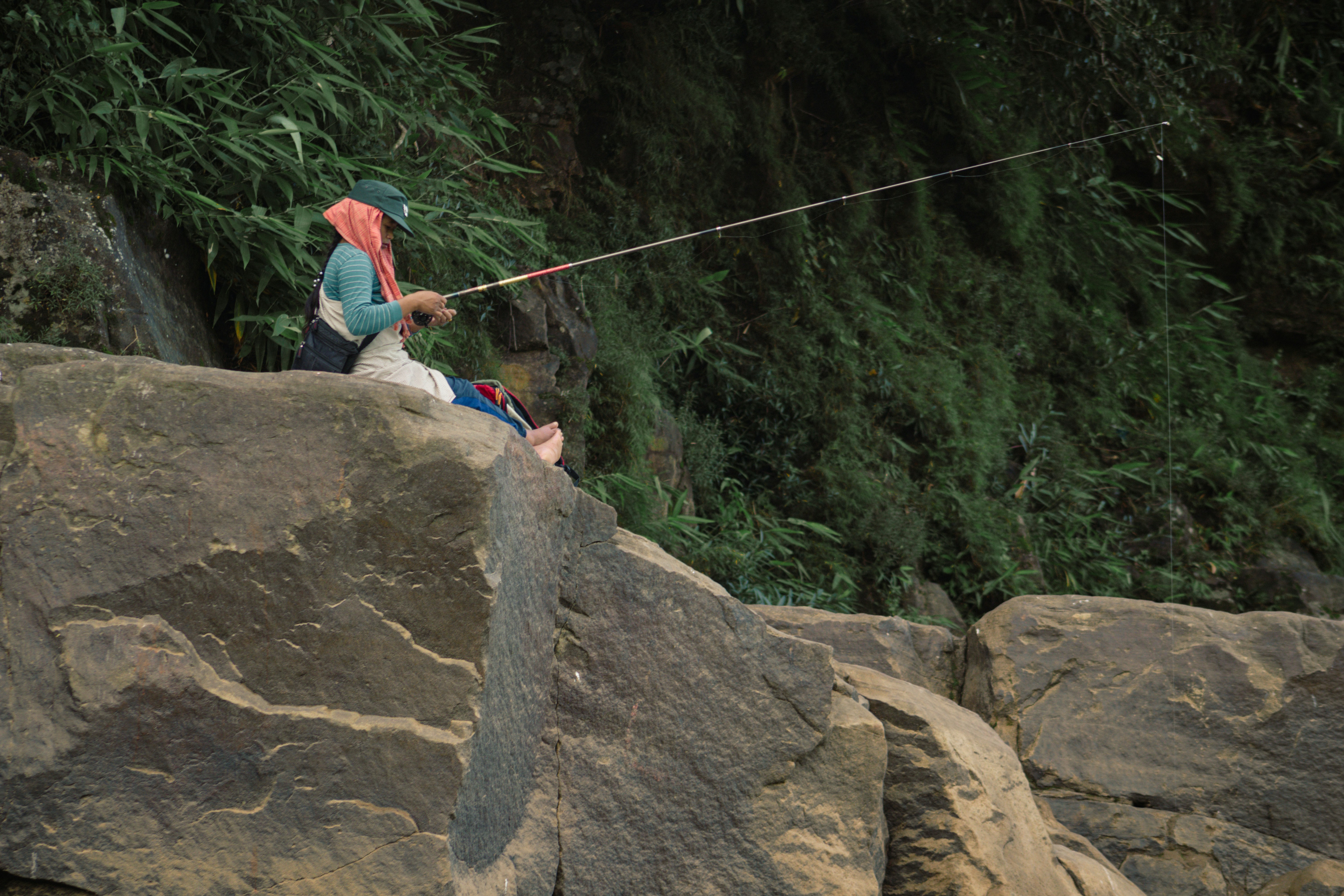 A person fishing with a rod while perched on a large rock