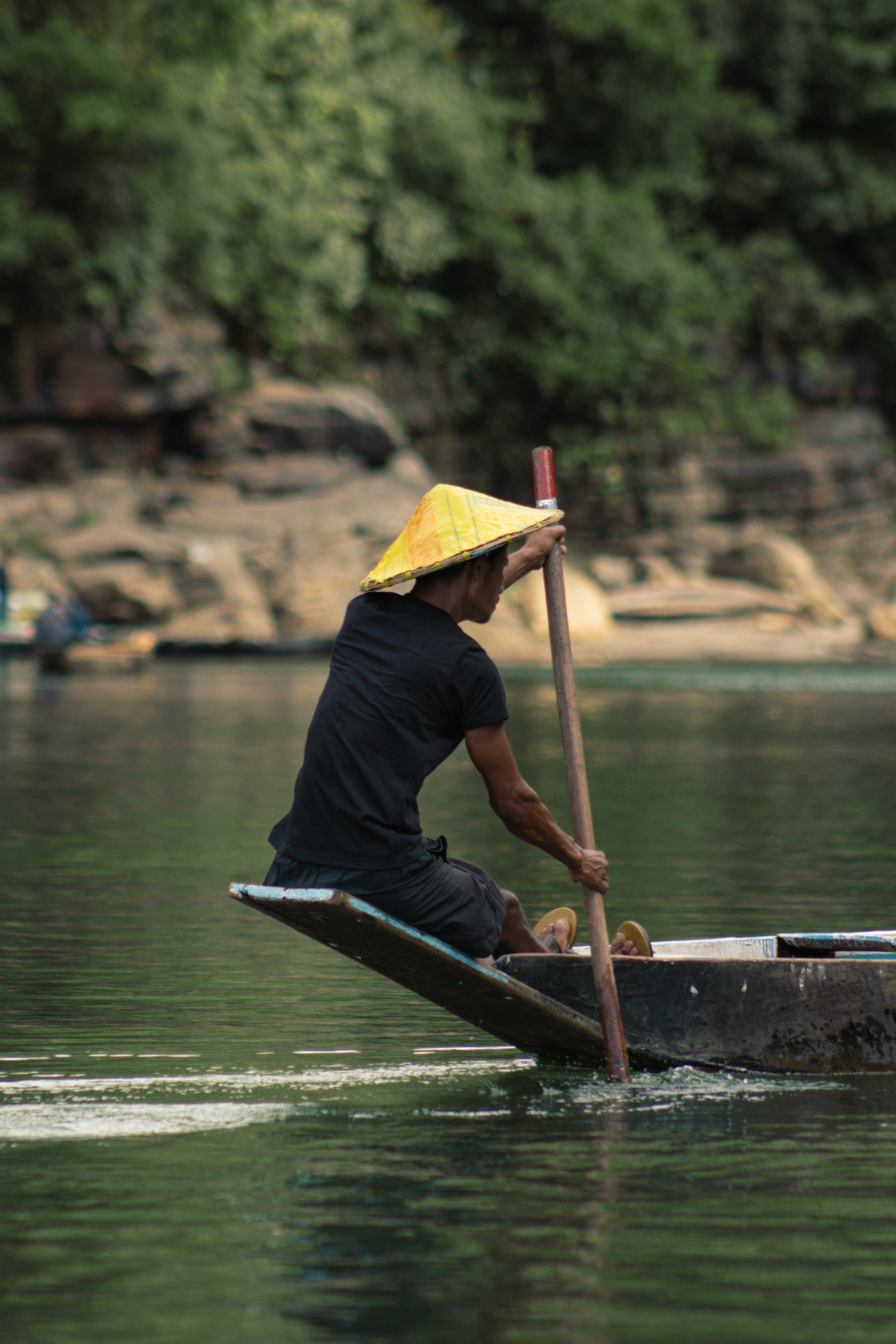 A person in a conical hat rowing a wooden boat on a river