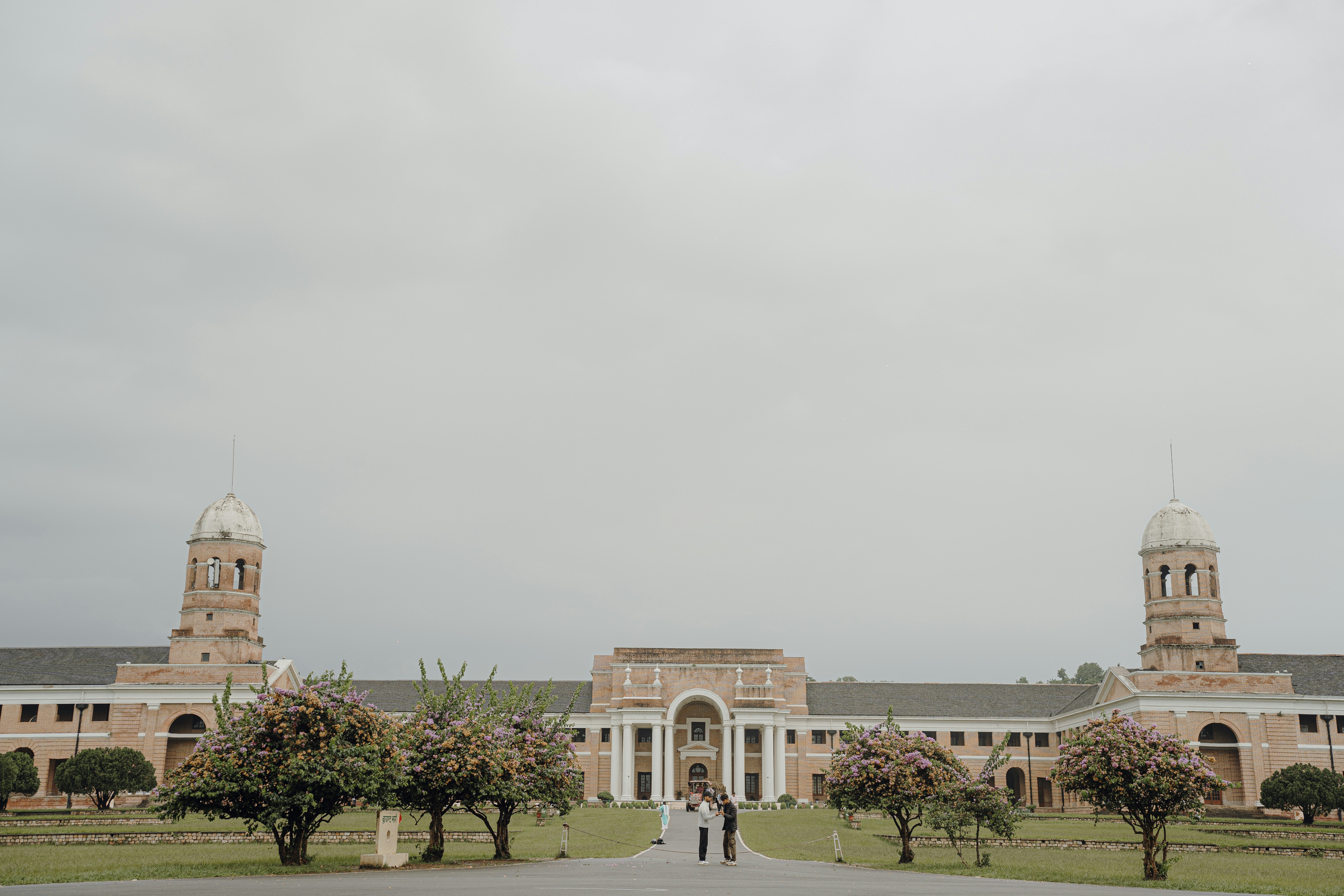 Grand building with towers and trees under cloudy sky.