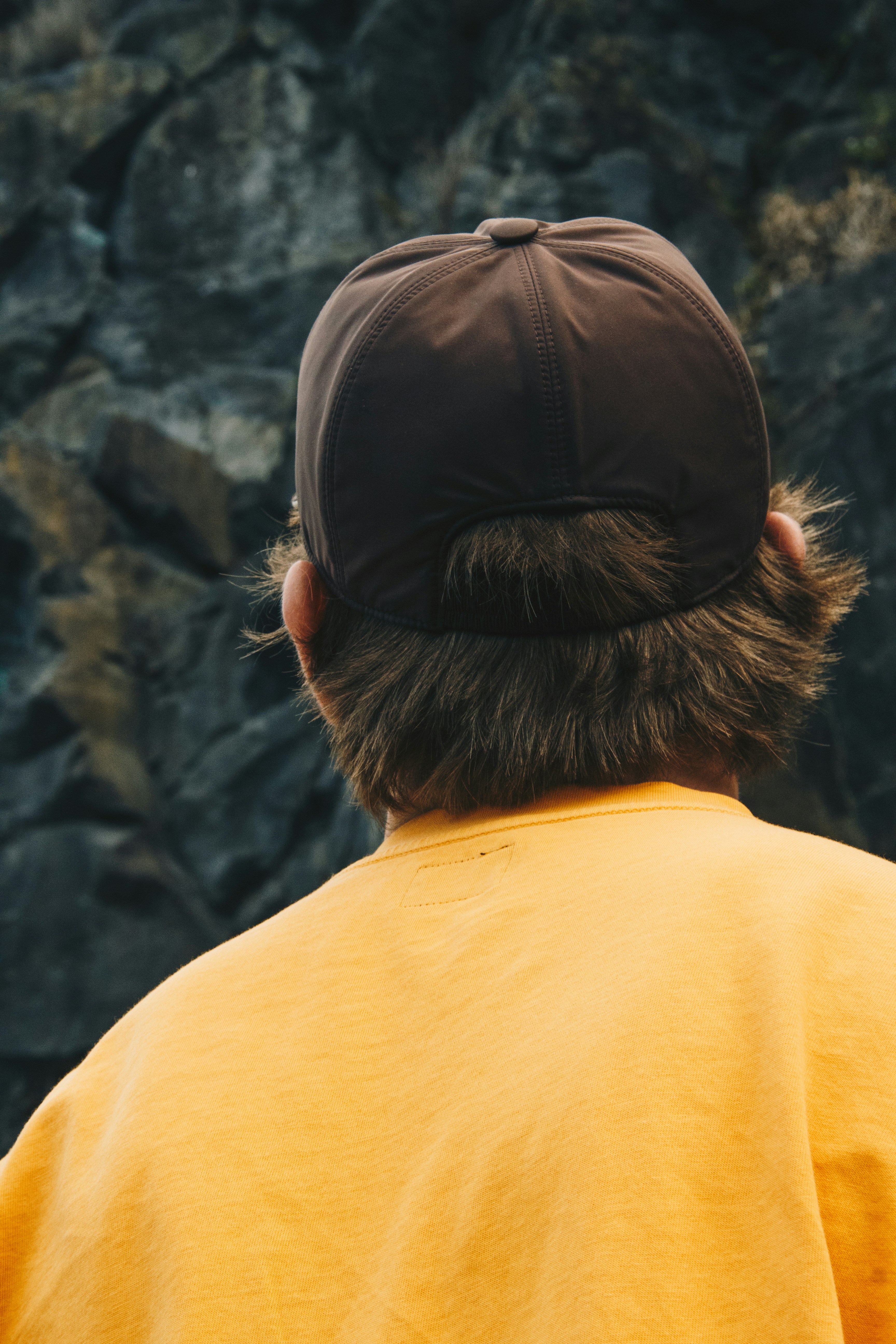 Back of person wearing a brown cap and yellow shirt
