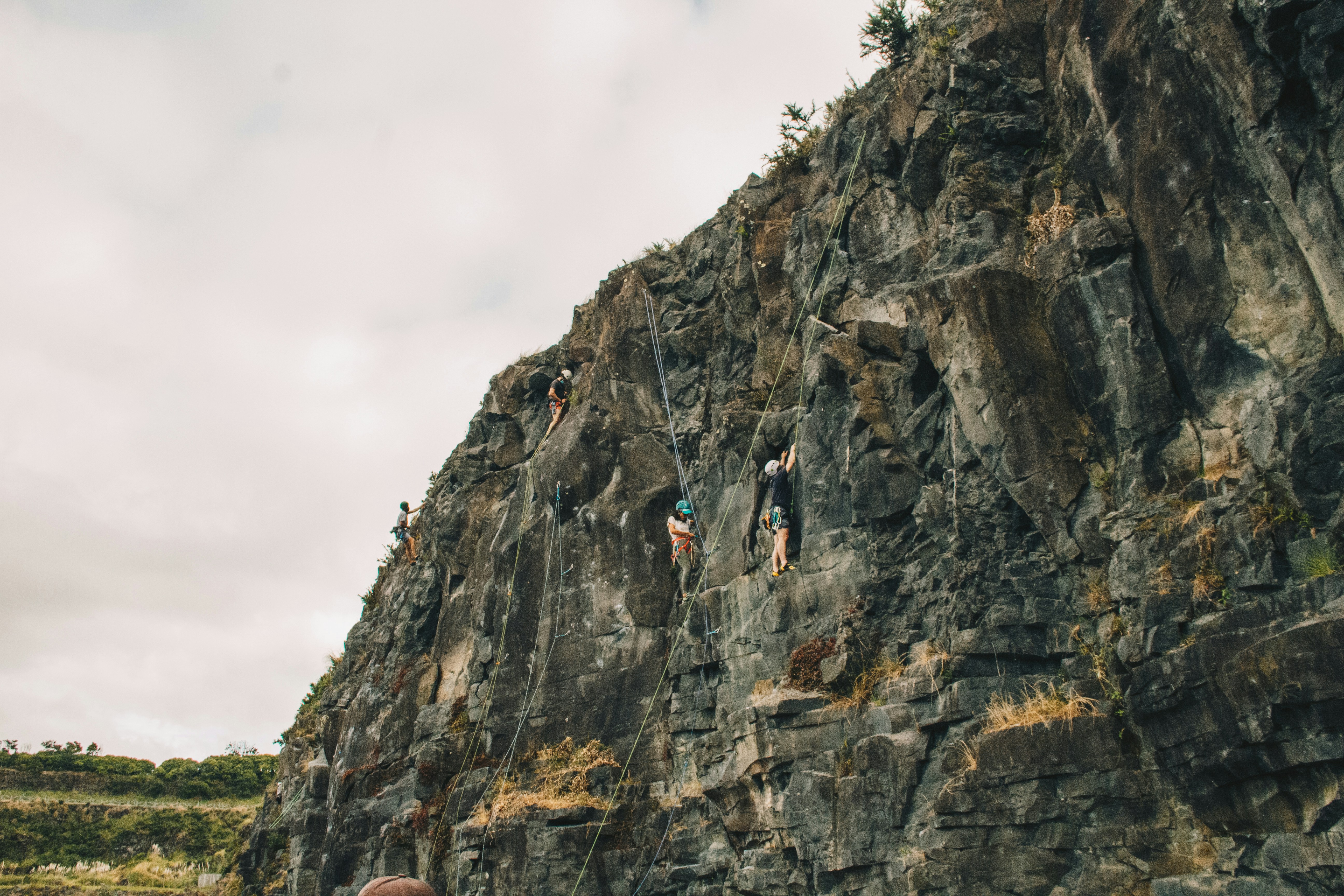 People rock climbing on a steep, grey cliff face.