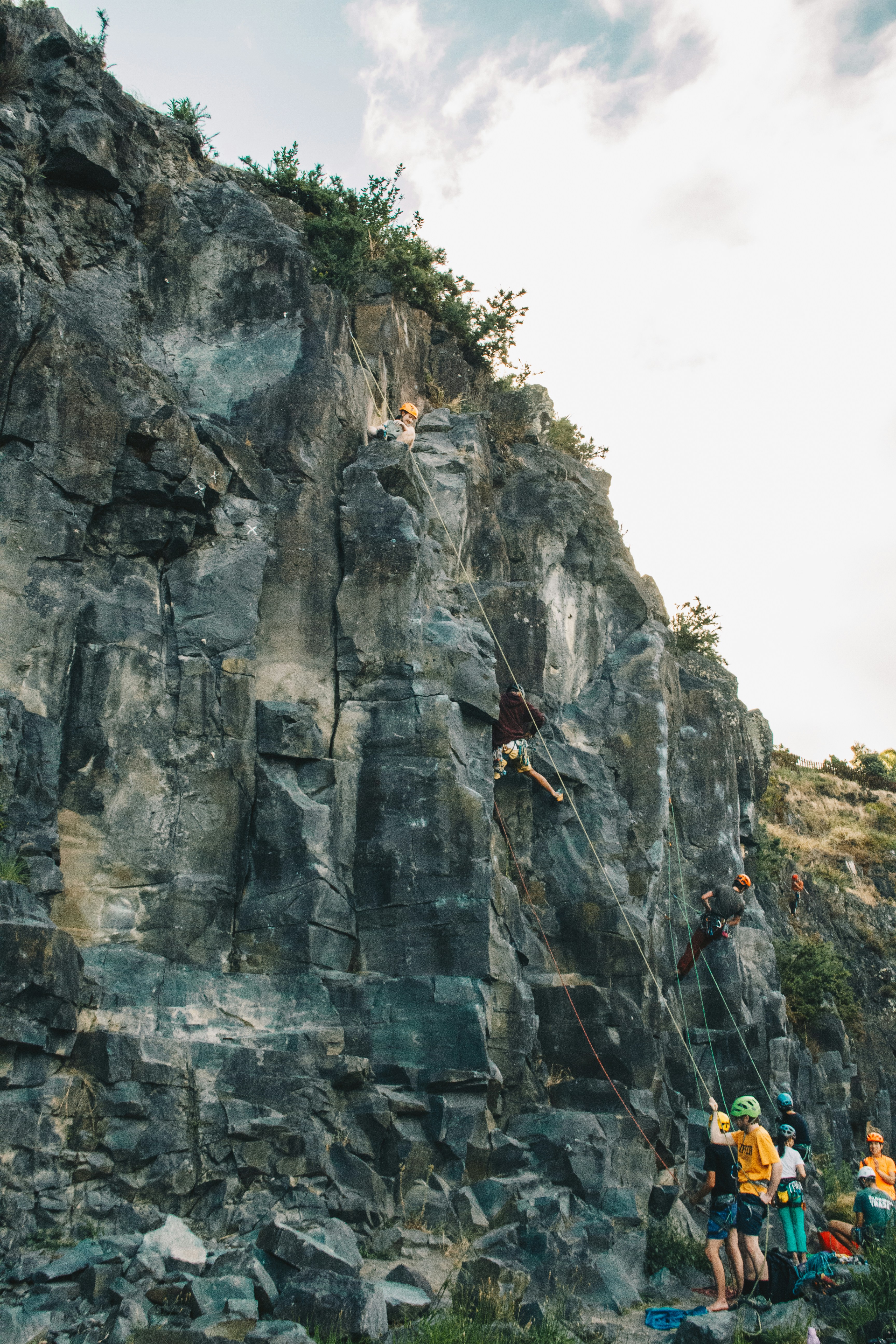 People rock climbing up a steep quarry cliff face.