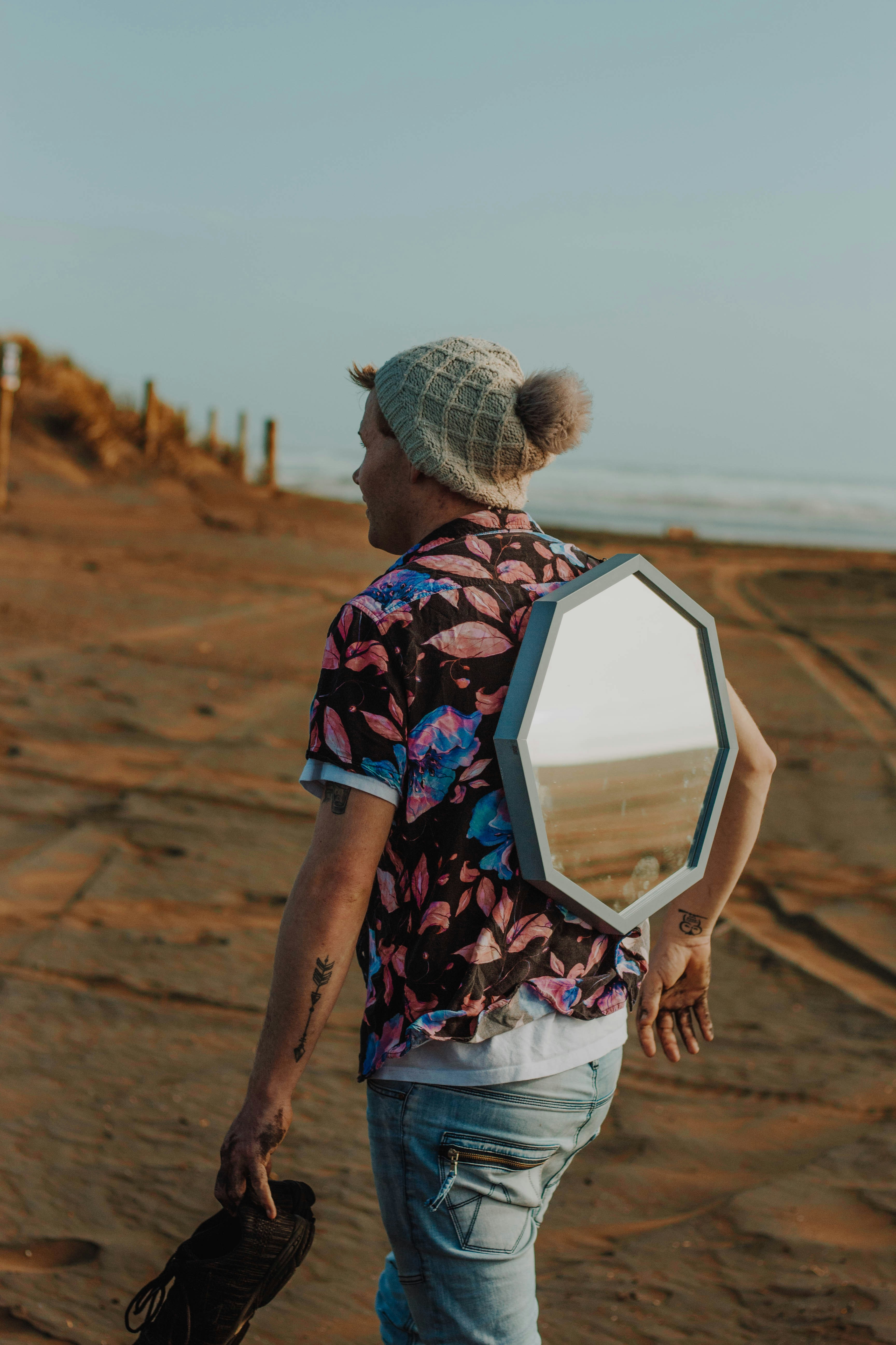 Man with mirror on back walks on sandy beach.