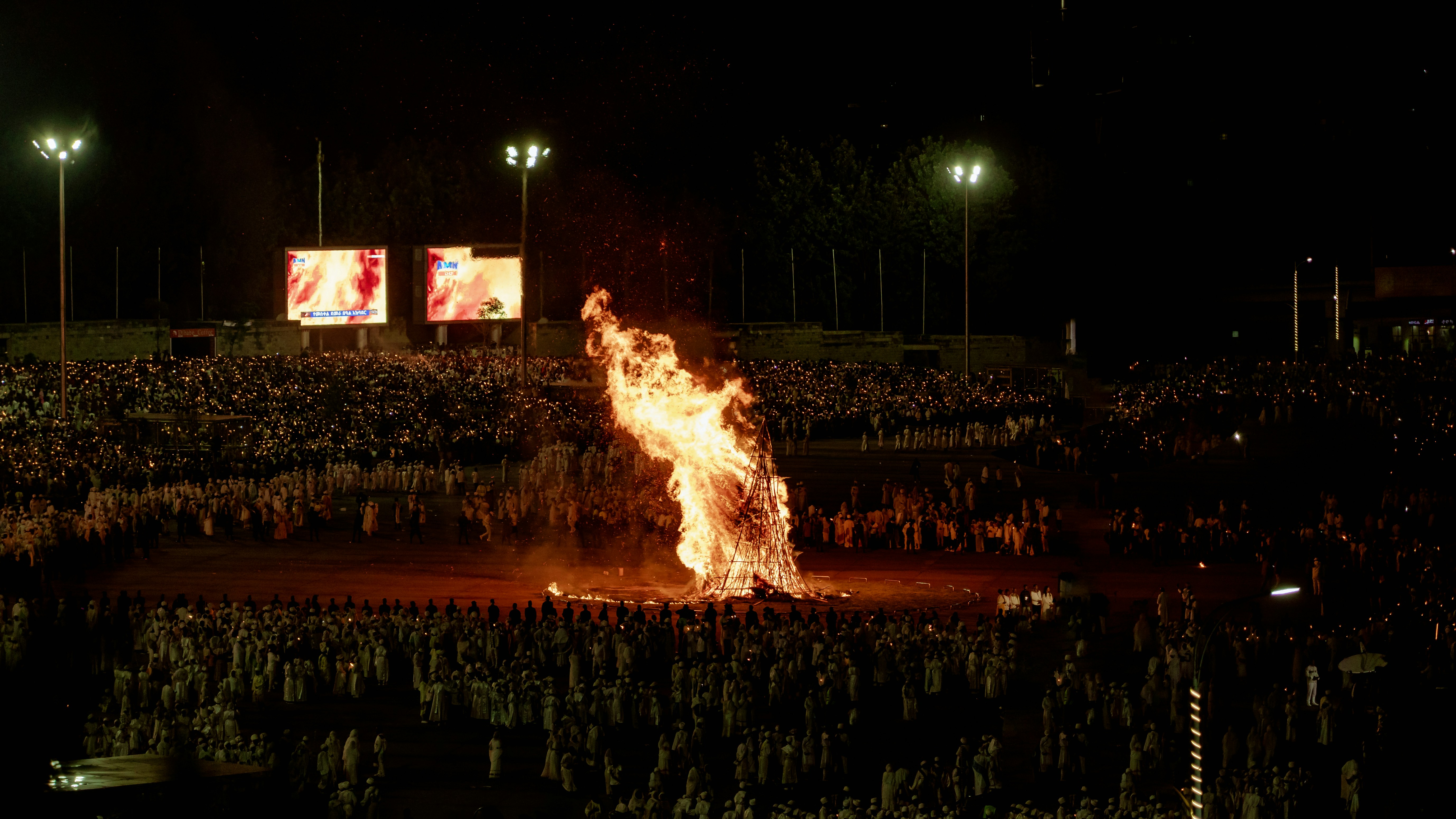 A large bonfire burns in a stadium at night.