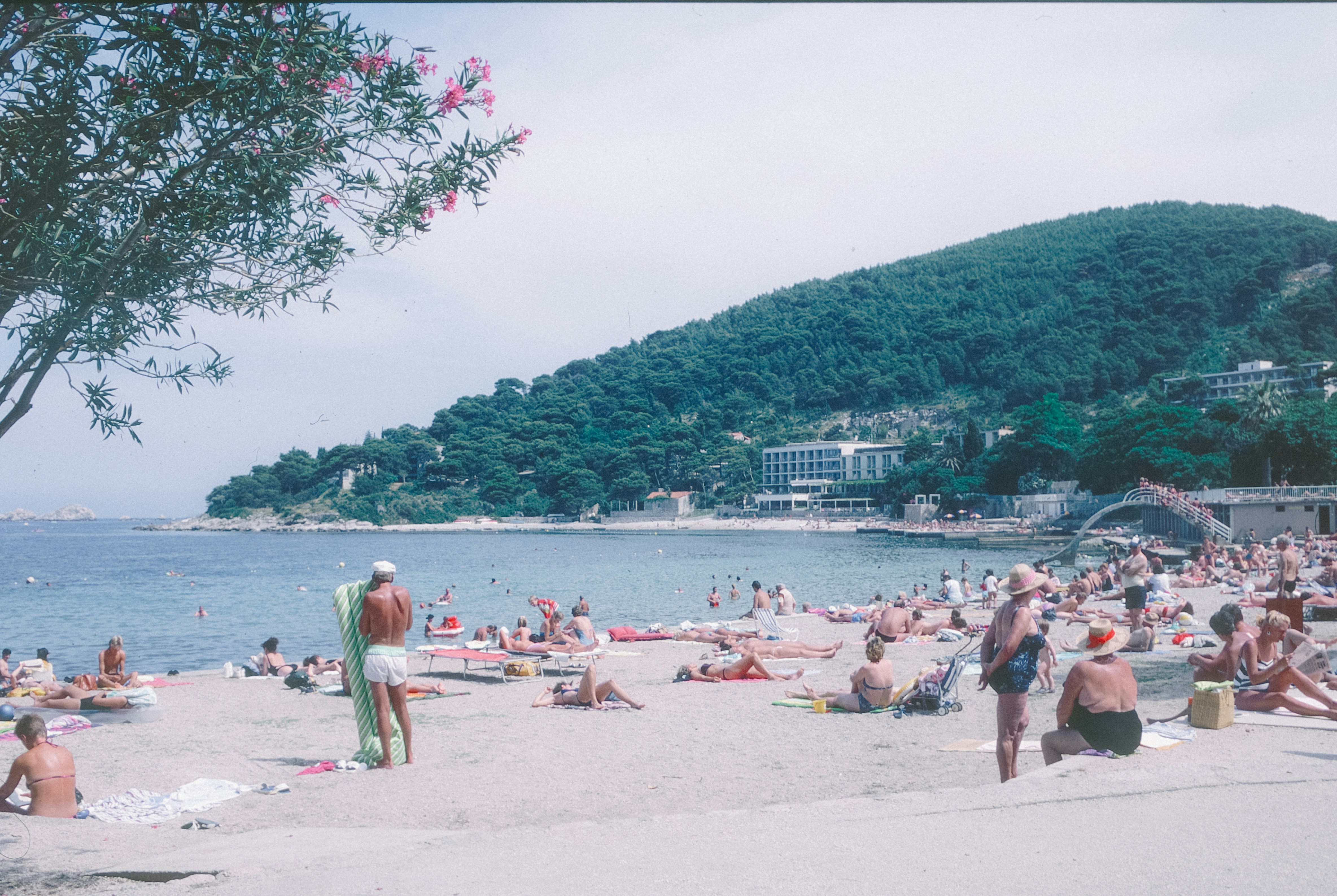 Crowded beach with people sunbathing and swimming in the ocean.