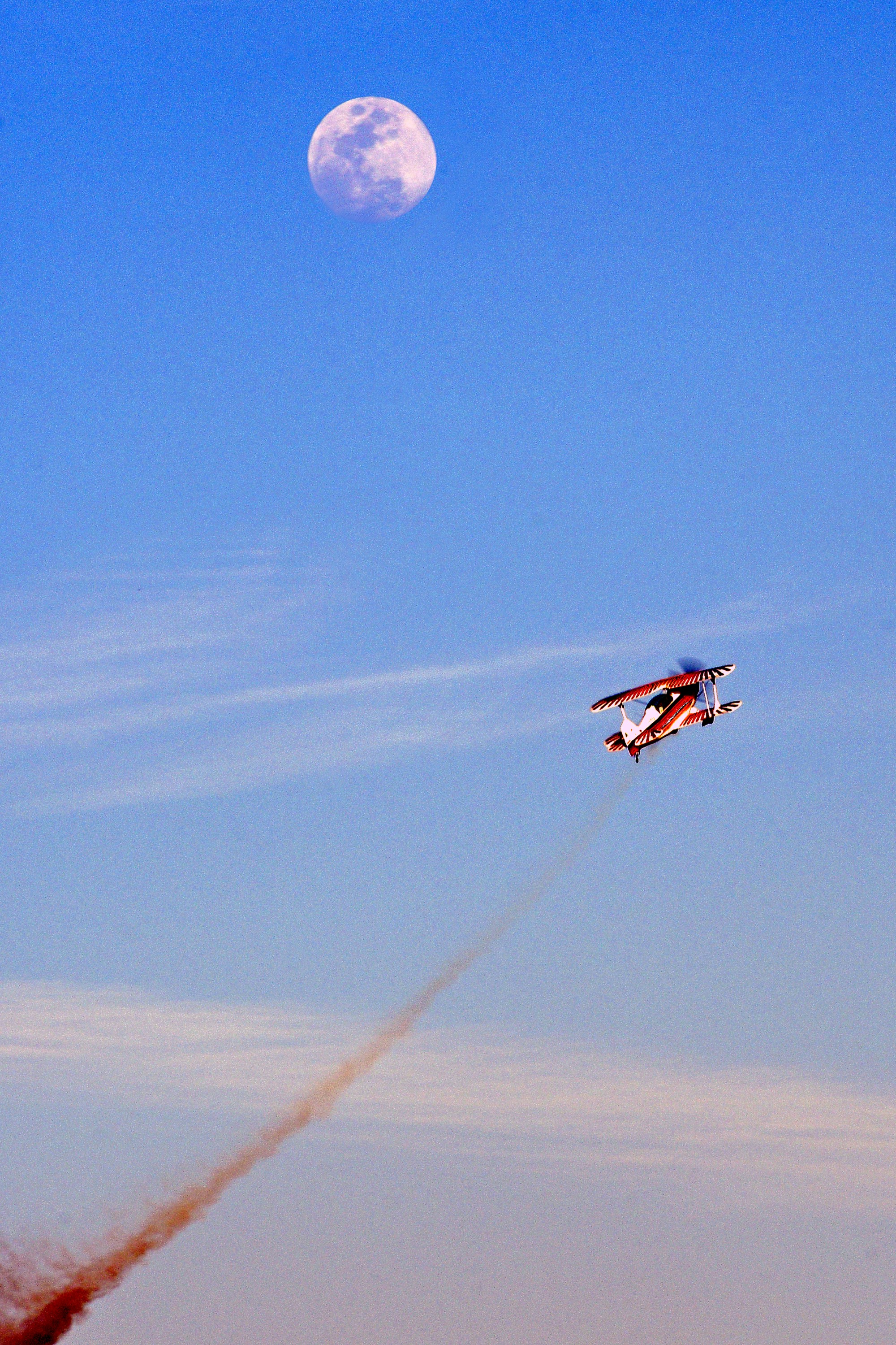 Biplane performs aerobatics with smoke trail under moon.
