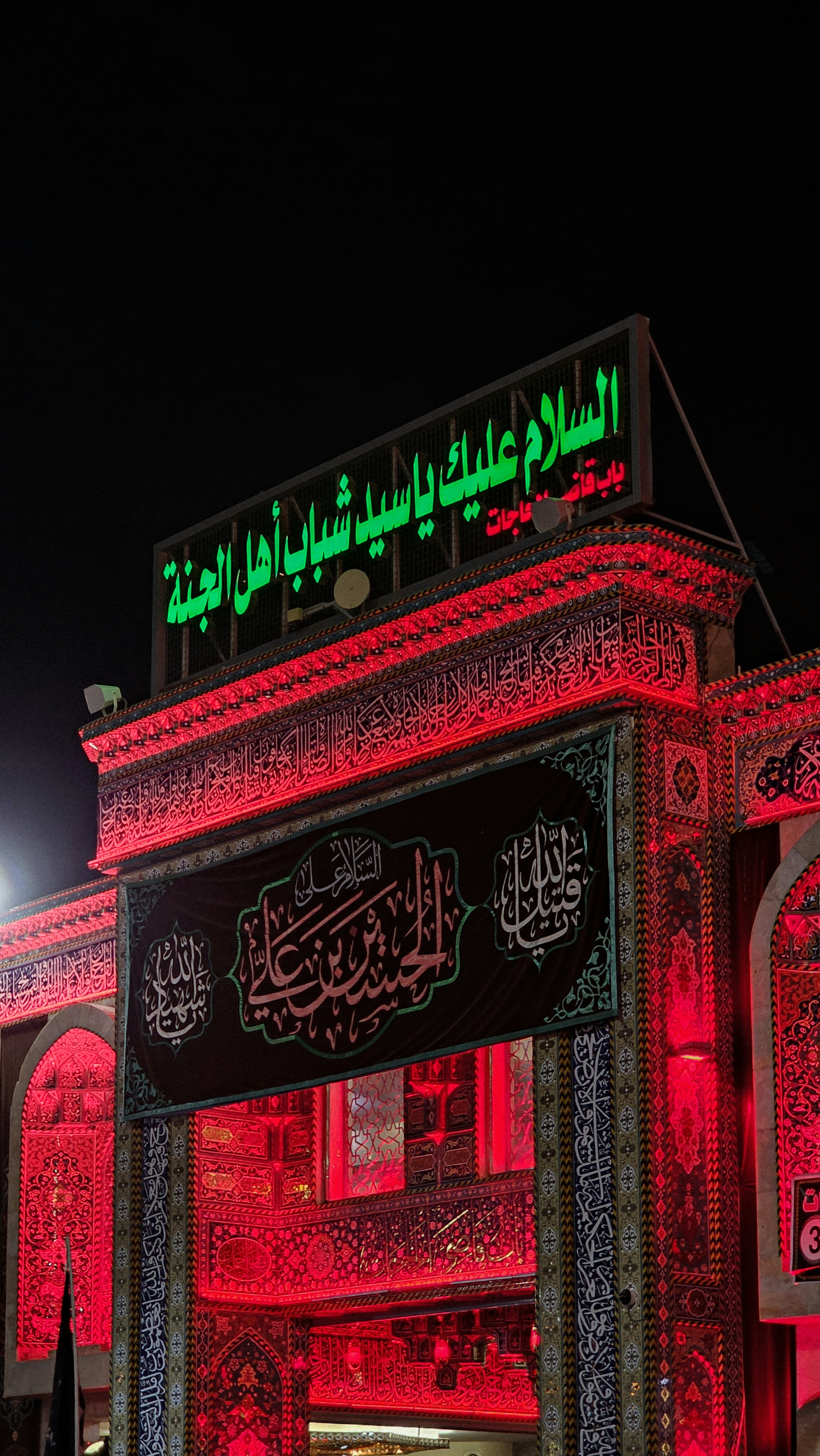 Entrée du bâtiment ornée éclairée par des lumières rouges la nuit.