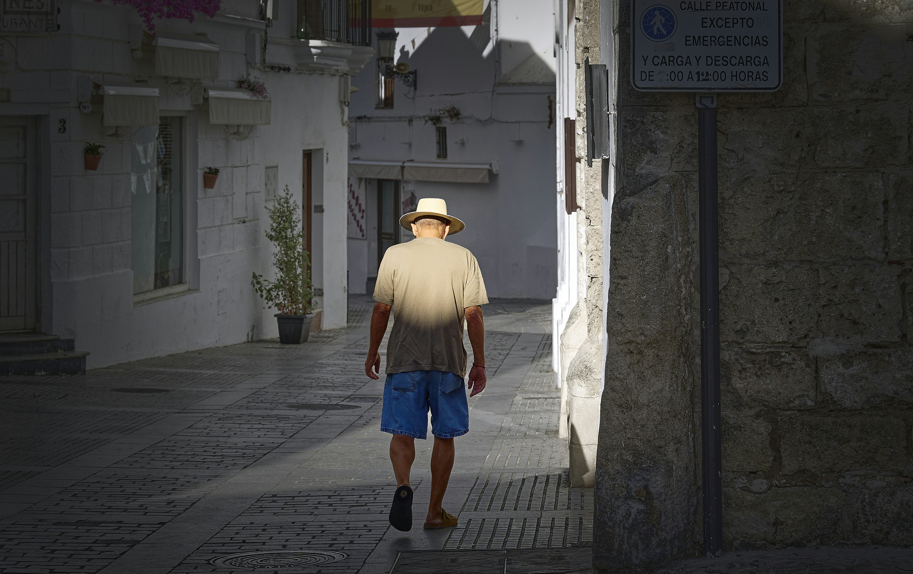Man in hat walks down sunlit street.