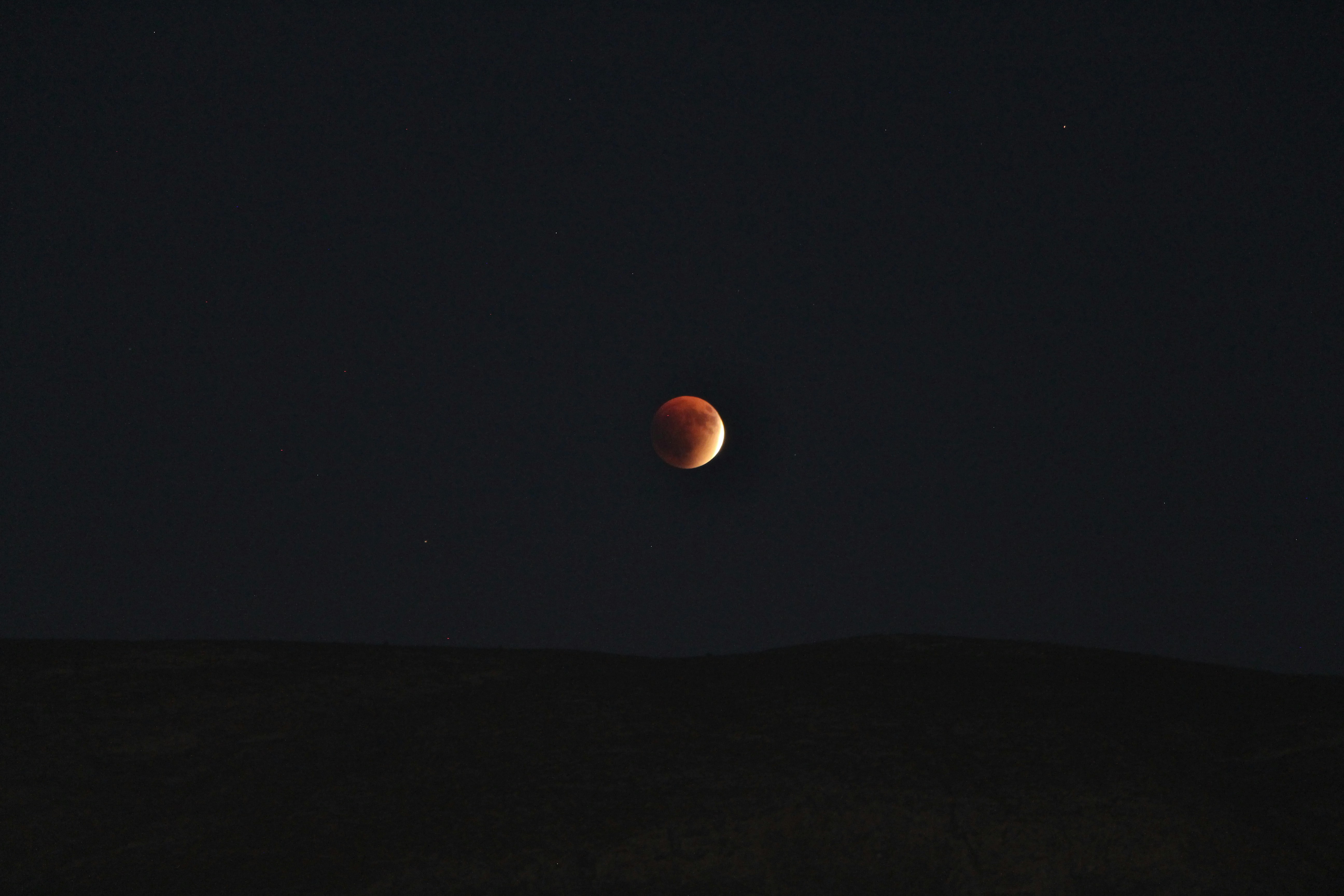 A blood moon eclipses the dark night sky.