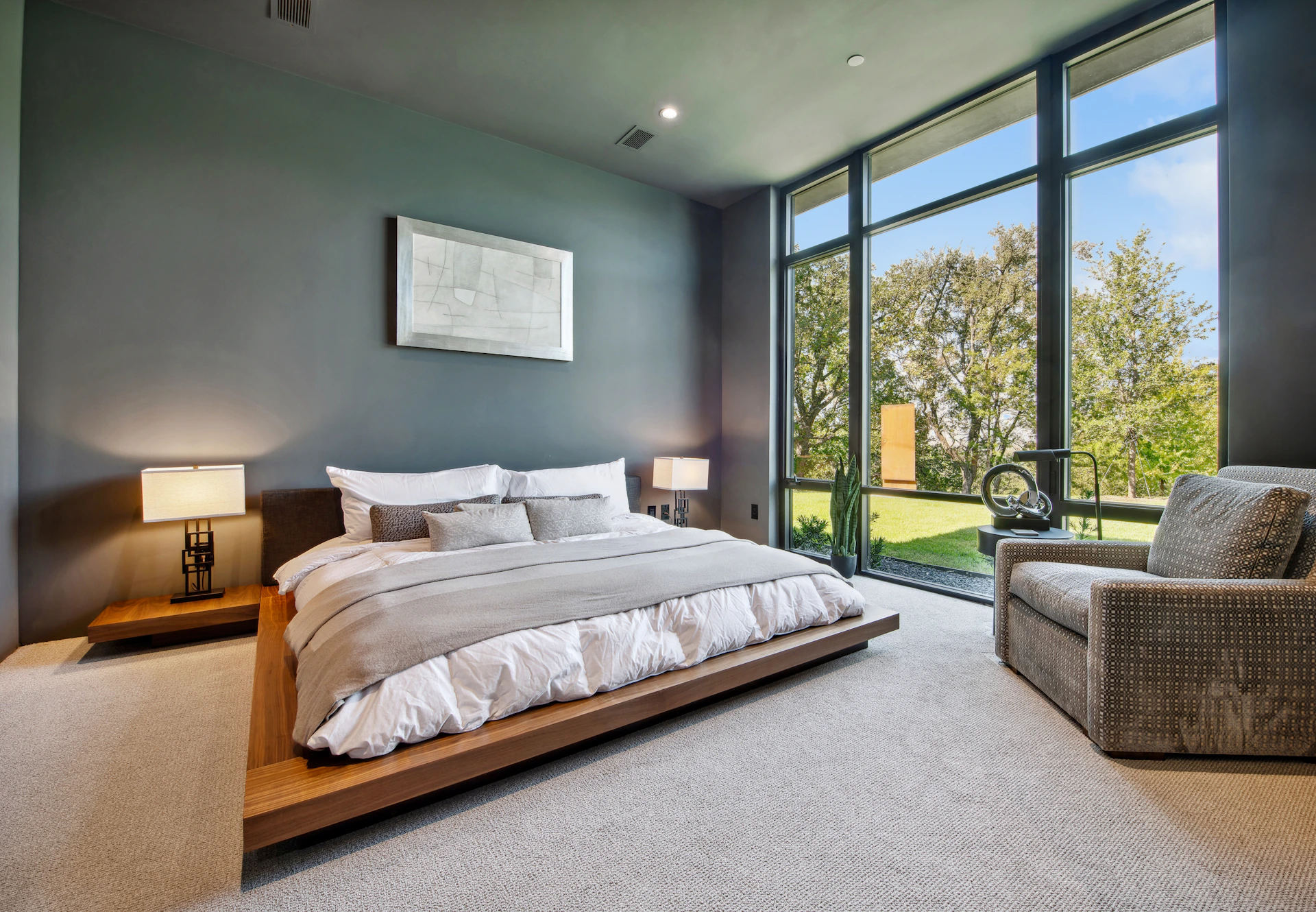 Modern bedroom with large window overlooking green lawn.