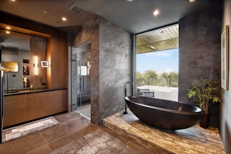 Modern bathroom with stone bathtub and large window.