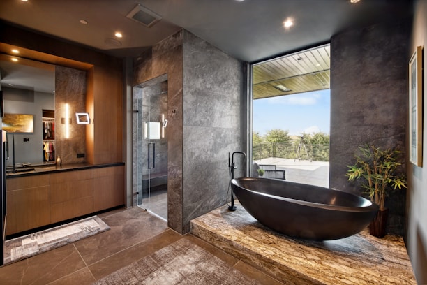 Modern bathroom with stone bathtub and large window.
