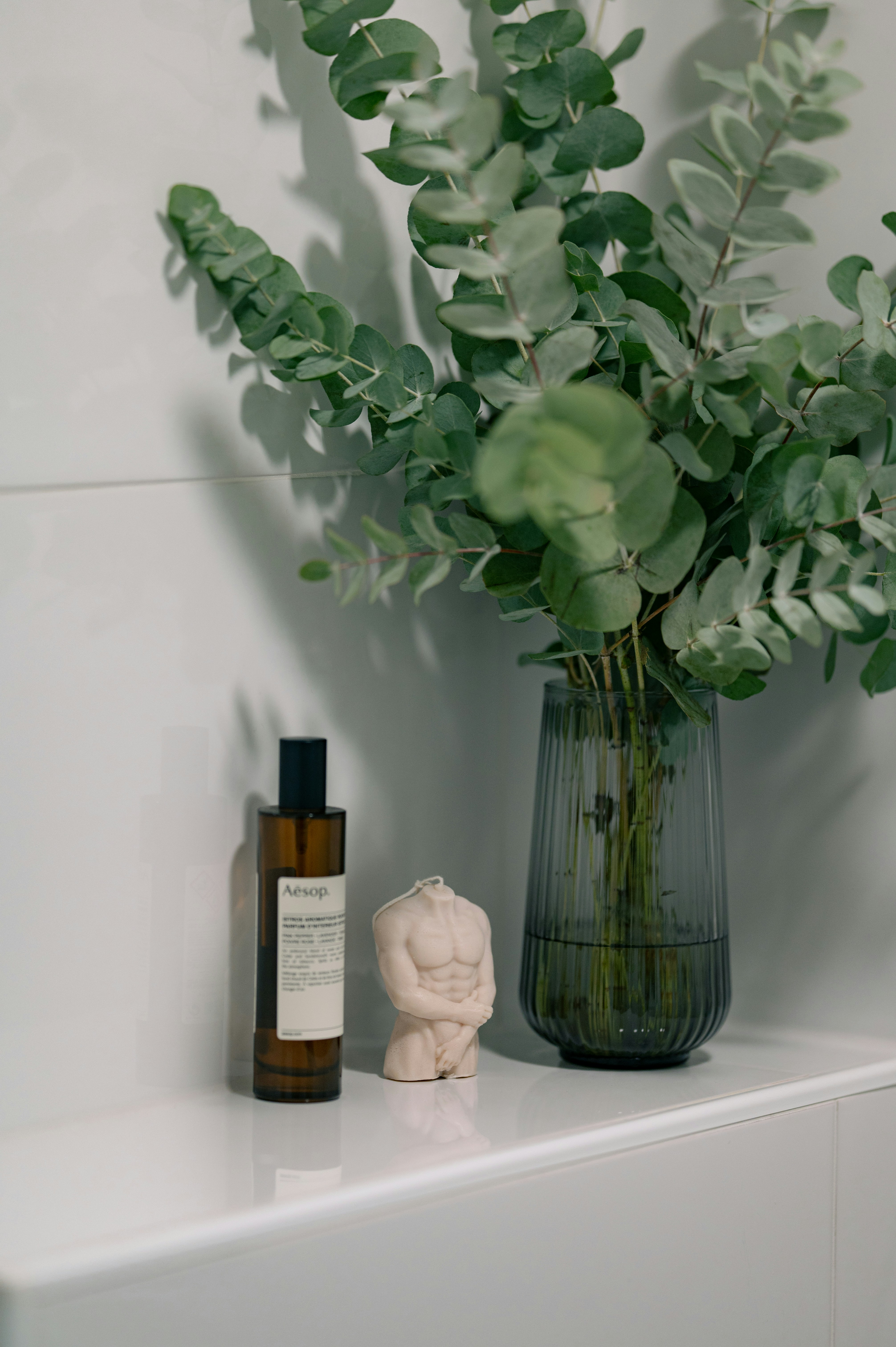 Eucalyptus branches in a vase with a candle and bottle.