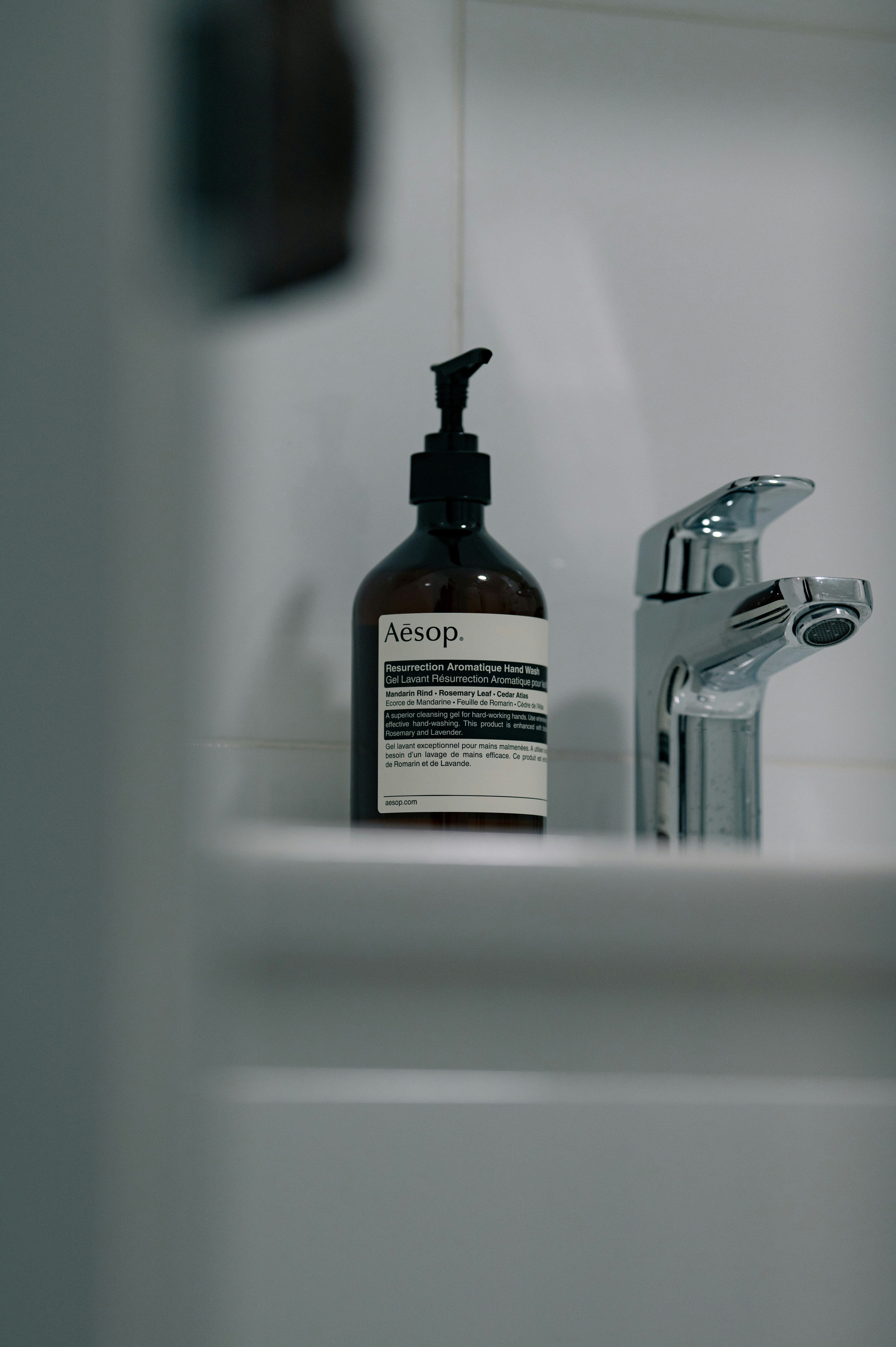 Aesop hand soap bottle next to a chrome faucet.