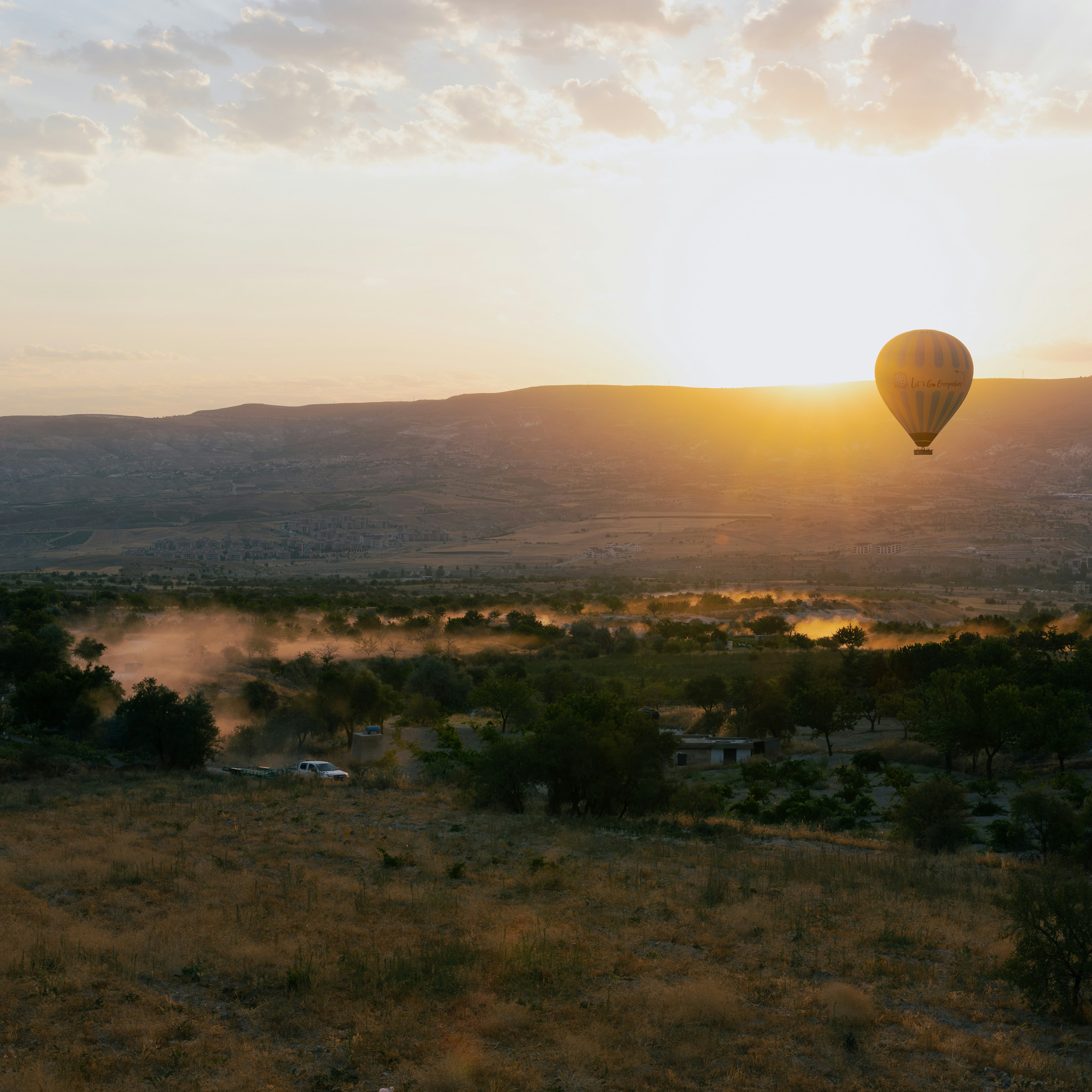Hot air balloon floats over landscape at sunrise.