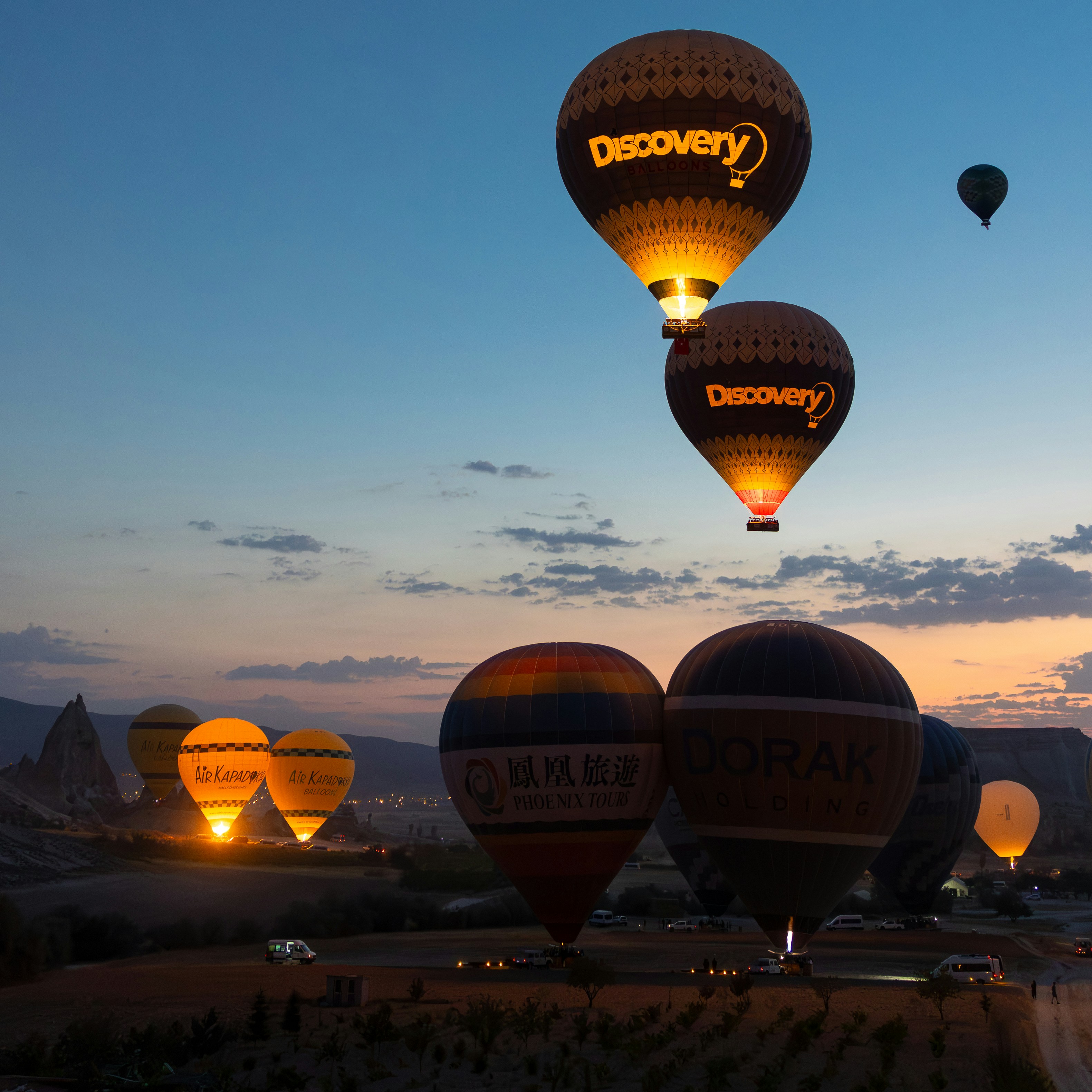 Hot air balloons glowing at sunrise over a landscape.