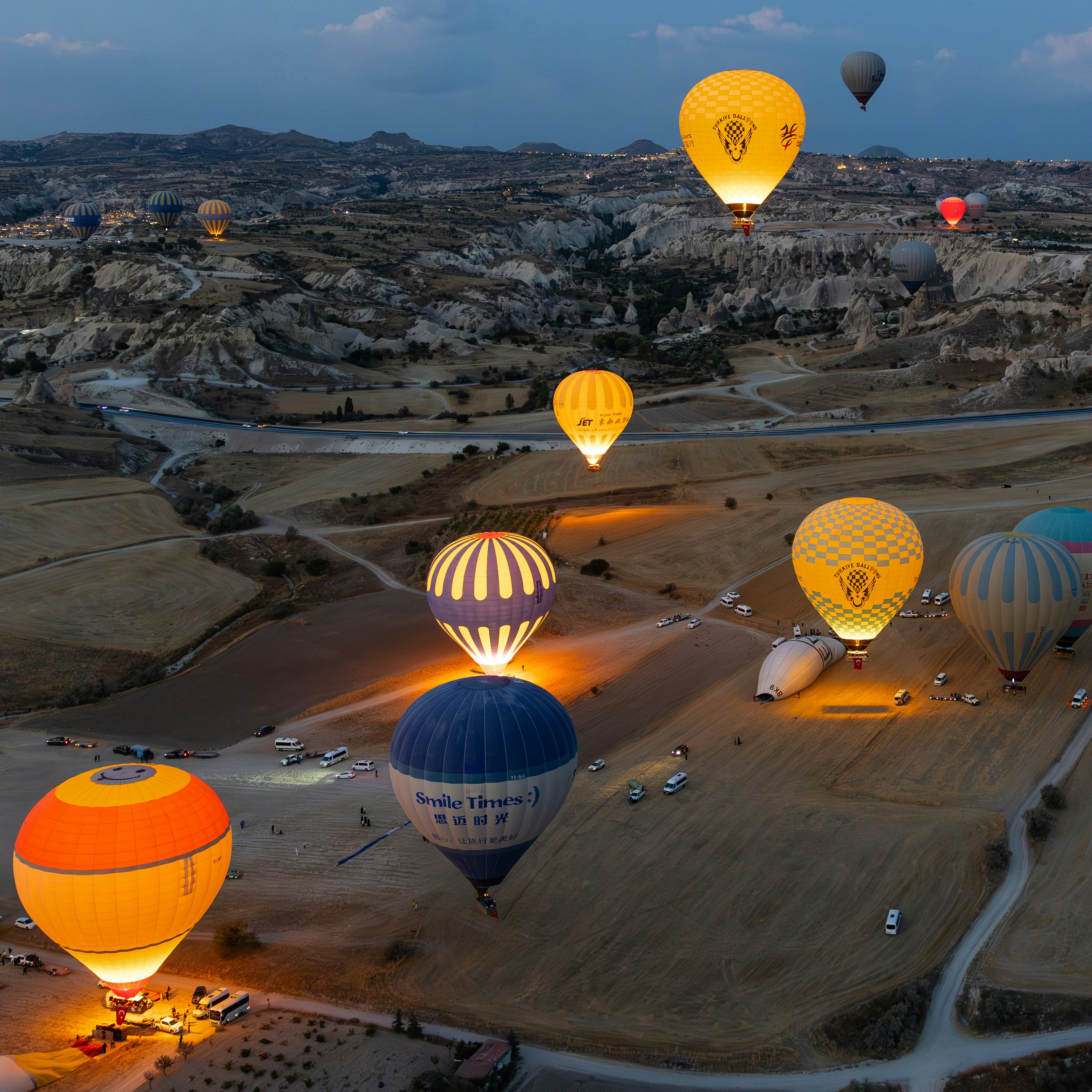 Hot air balloons ascend over rocky landscape at dawn.