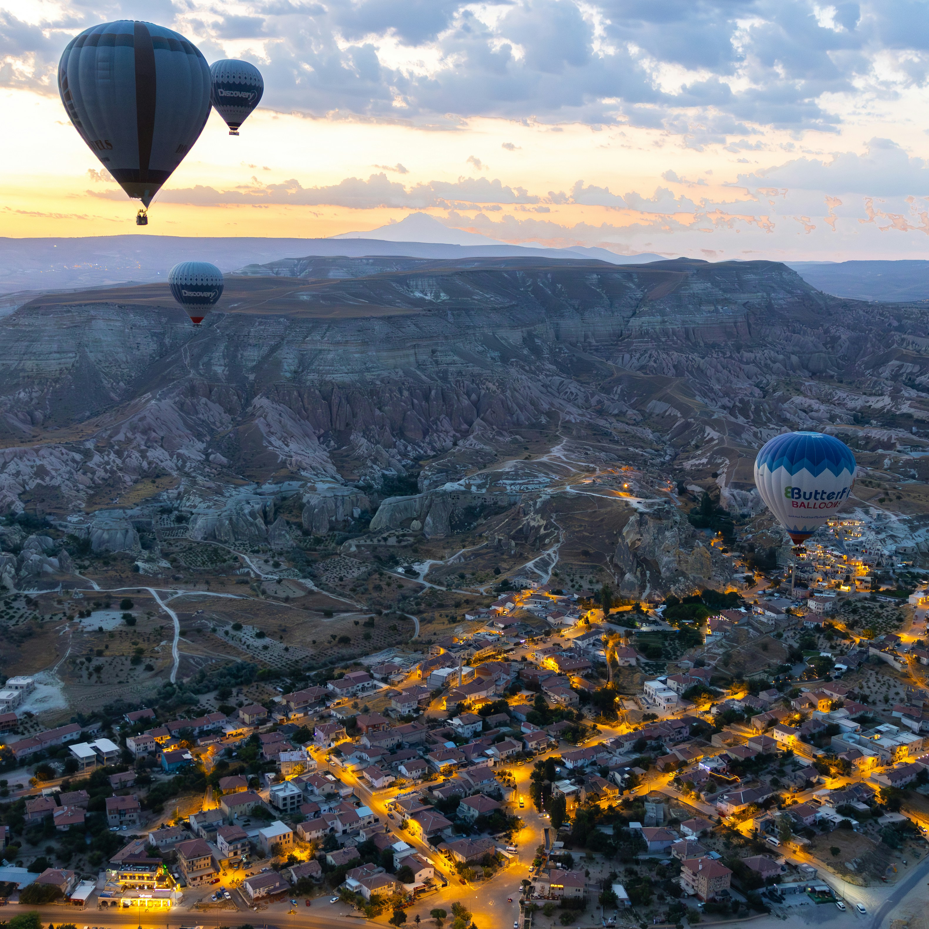 Hot air balloons fly over a town at sunrise.