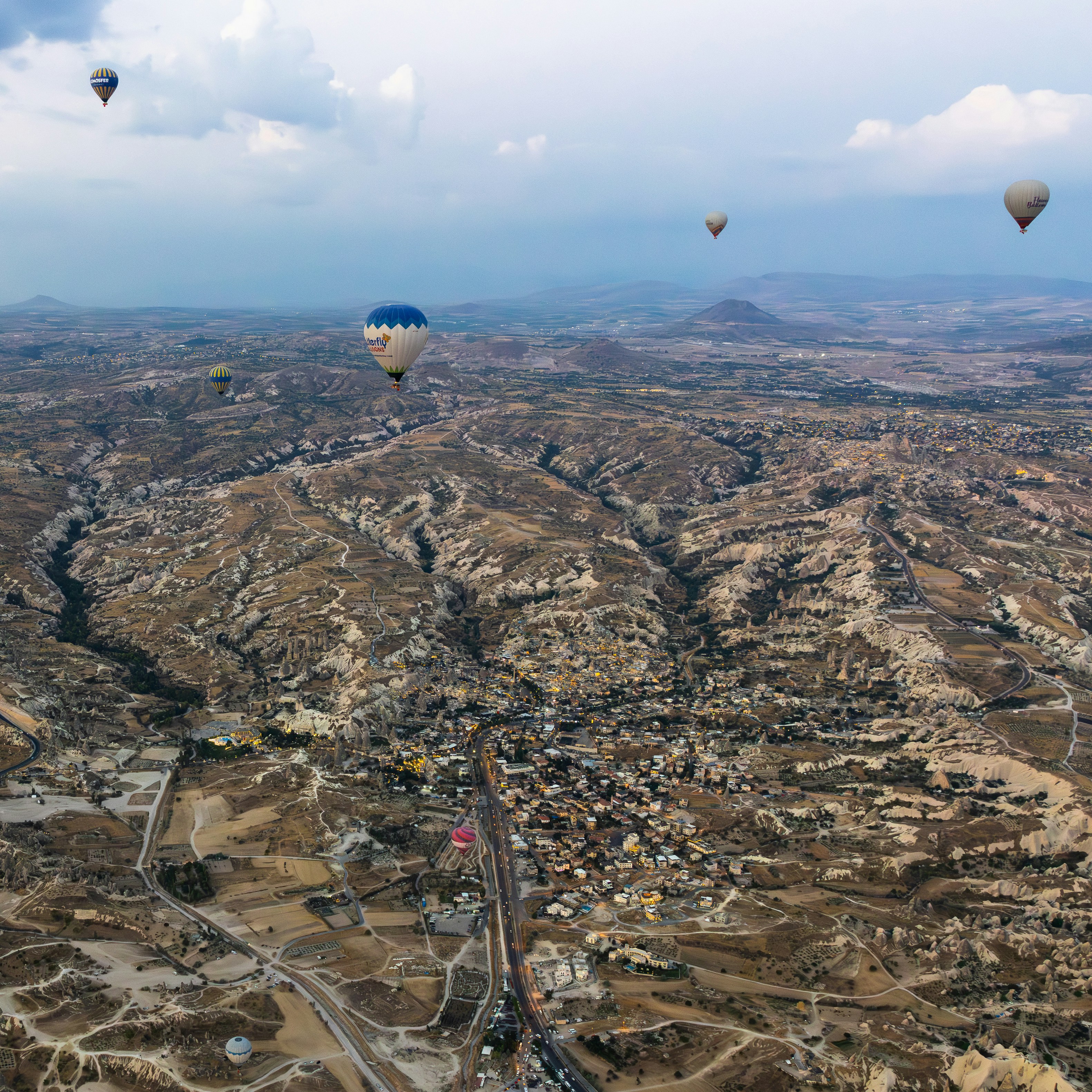 Hot air balloons float over a rocky, arid landscape.