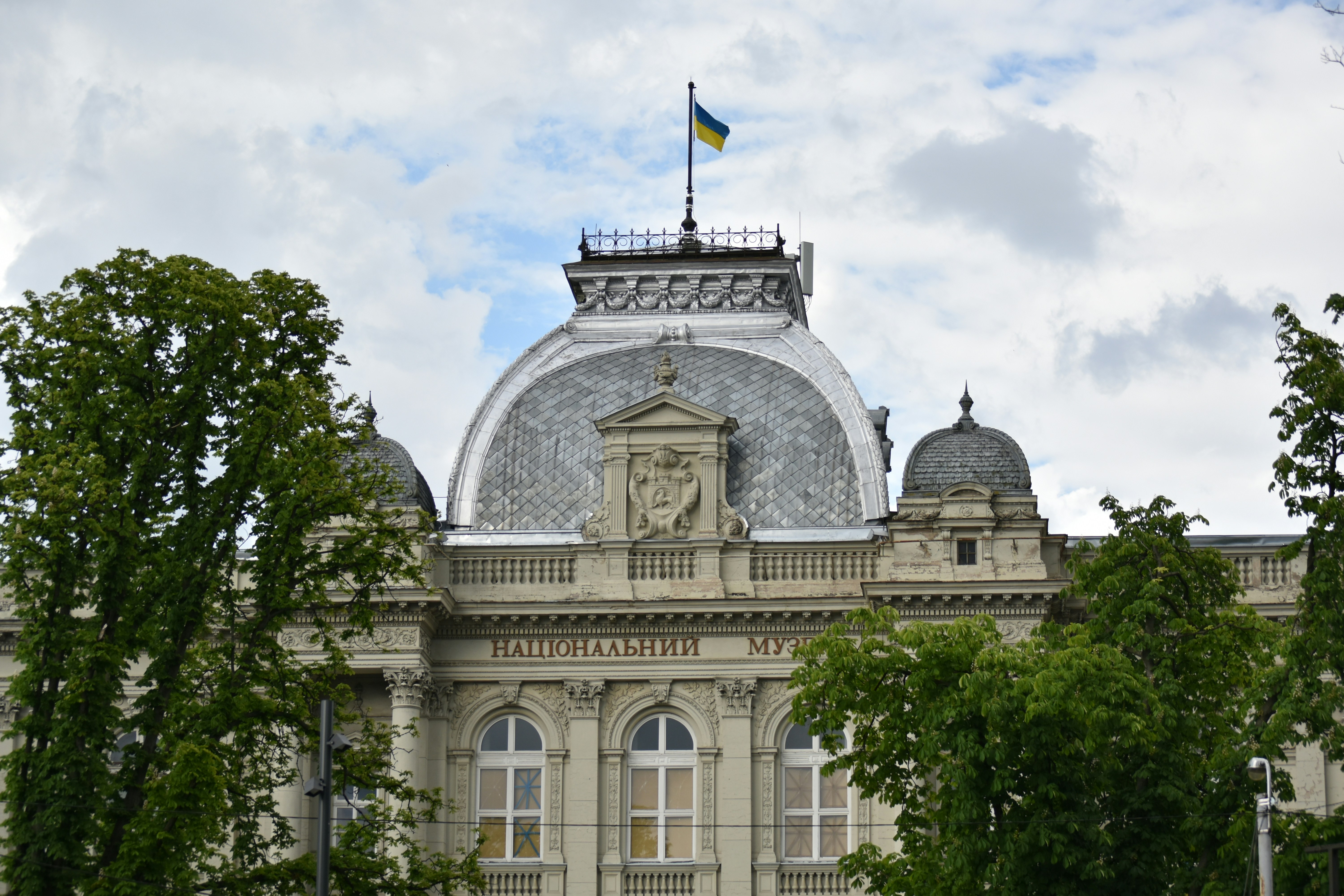 Ornate building with ukrainian flag under cloudy sky.