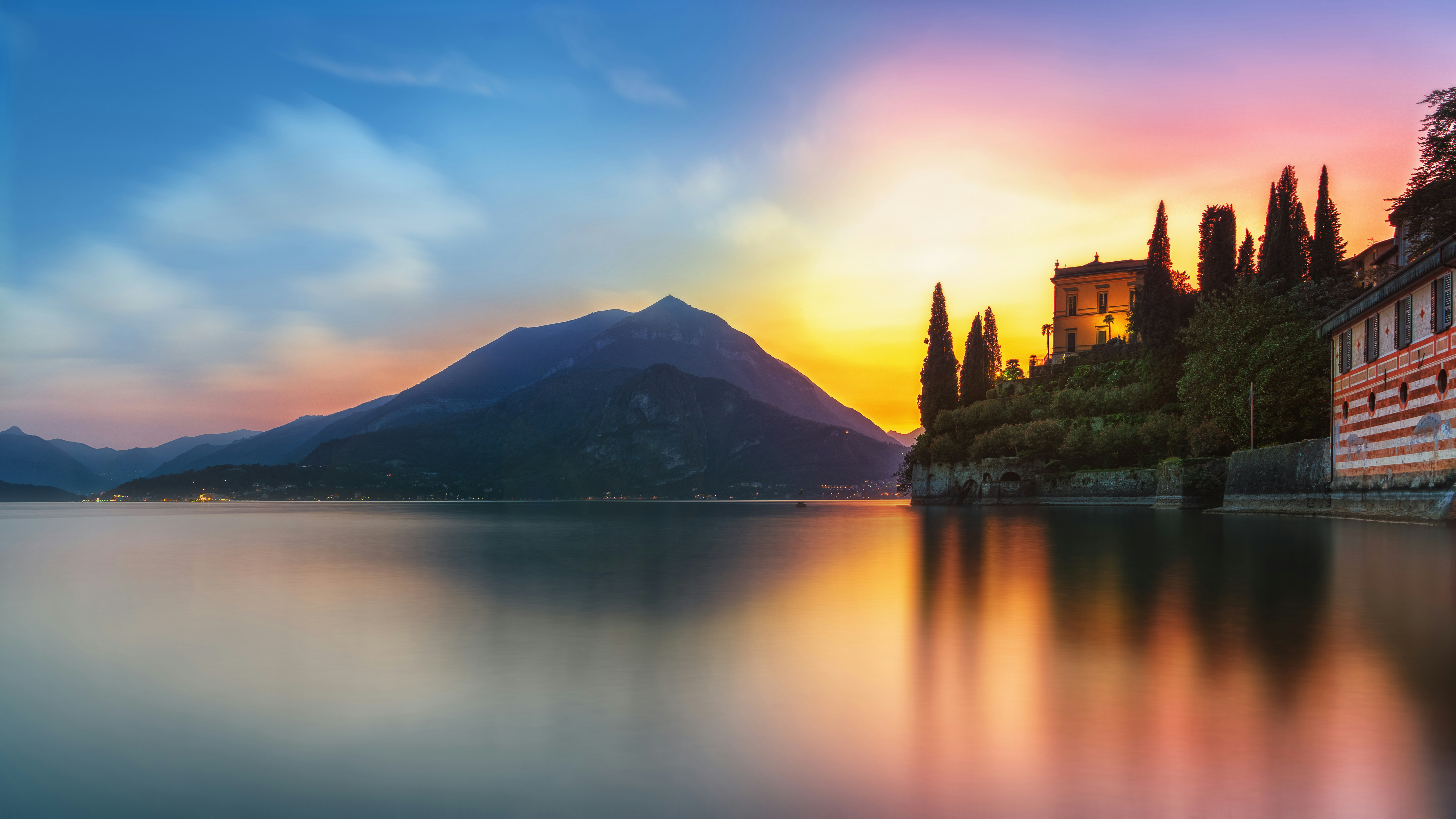 Sonnenuntergang über einem ruhigen See mit Bergen und Gebäuden.
