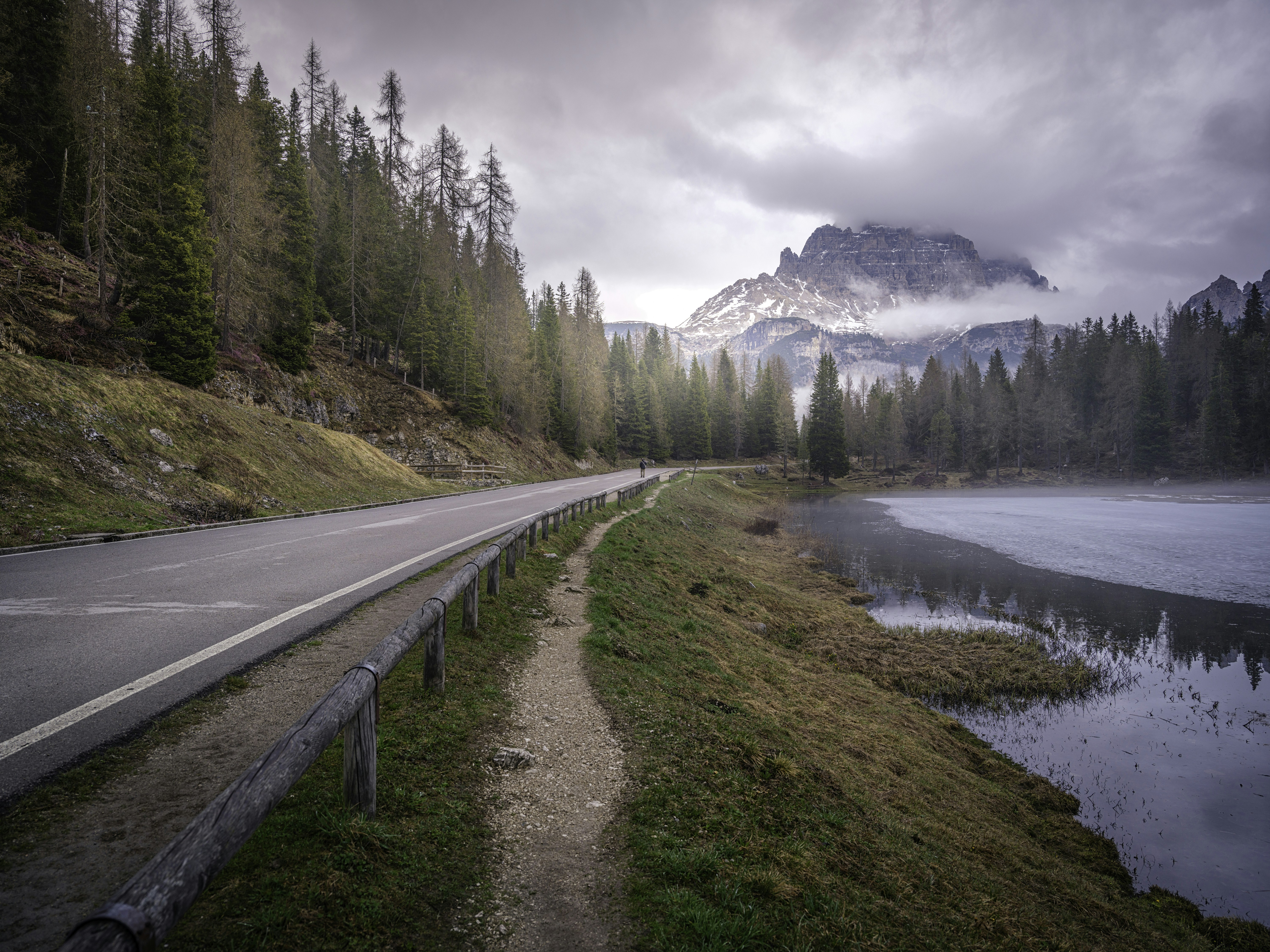 Bergstraße entlang eines nebligen Sees mit Kiefern.