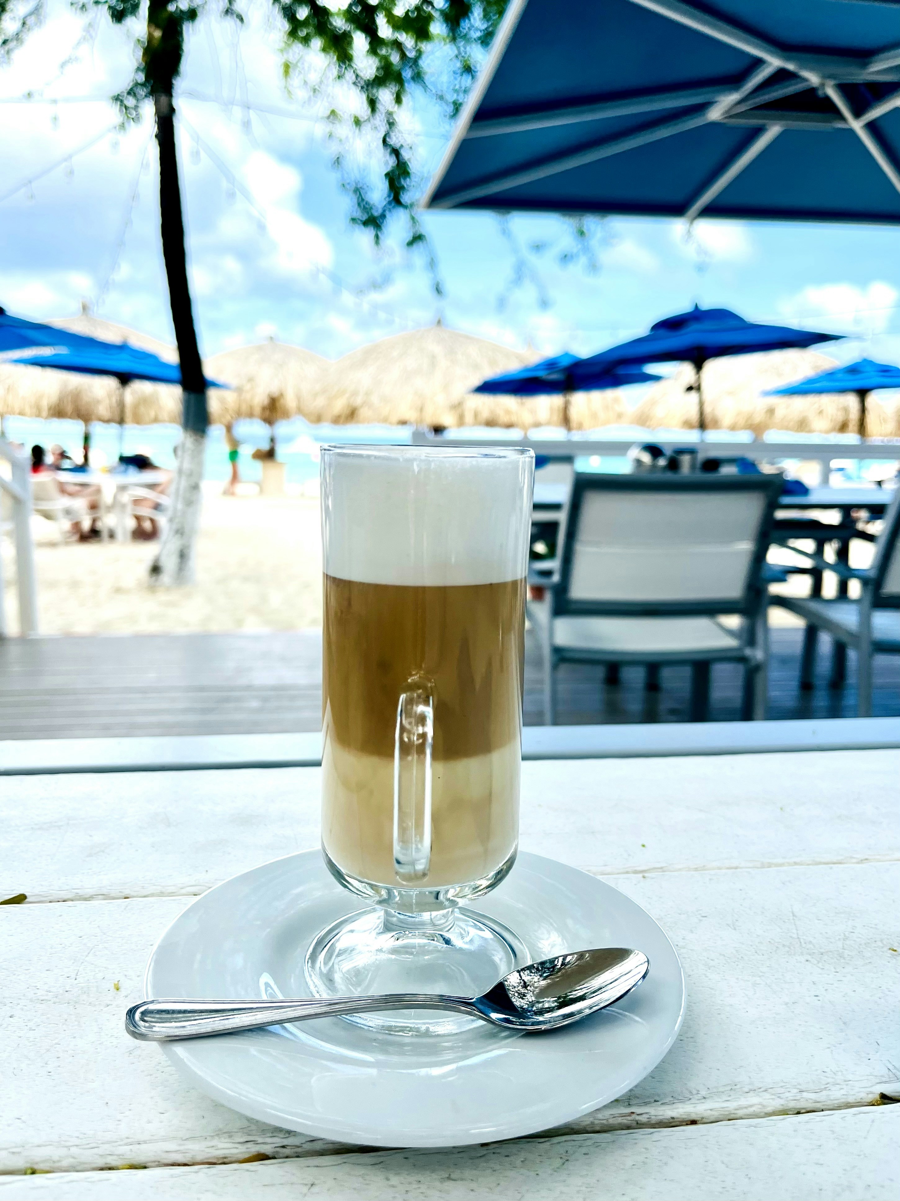 Schichtiges Kaffeegetränk auf einer Untertasse mit Löffel.