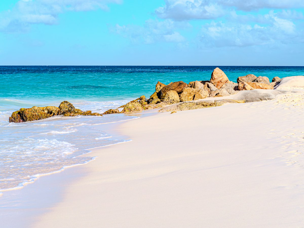 Sandy beach with rocks and turquoise ocean waves — calm swimming water
