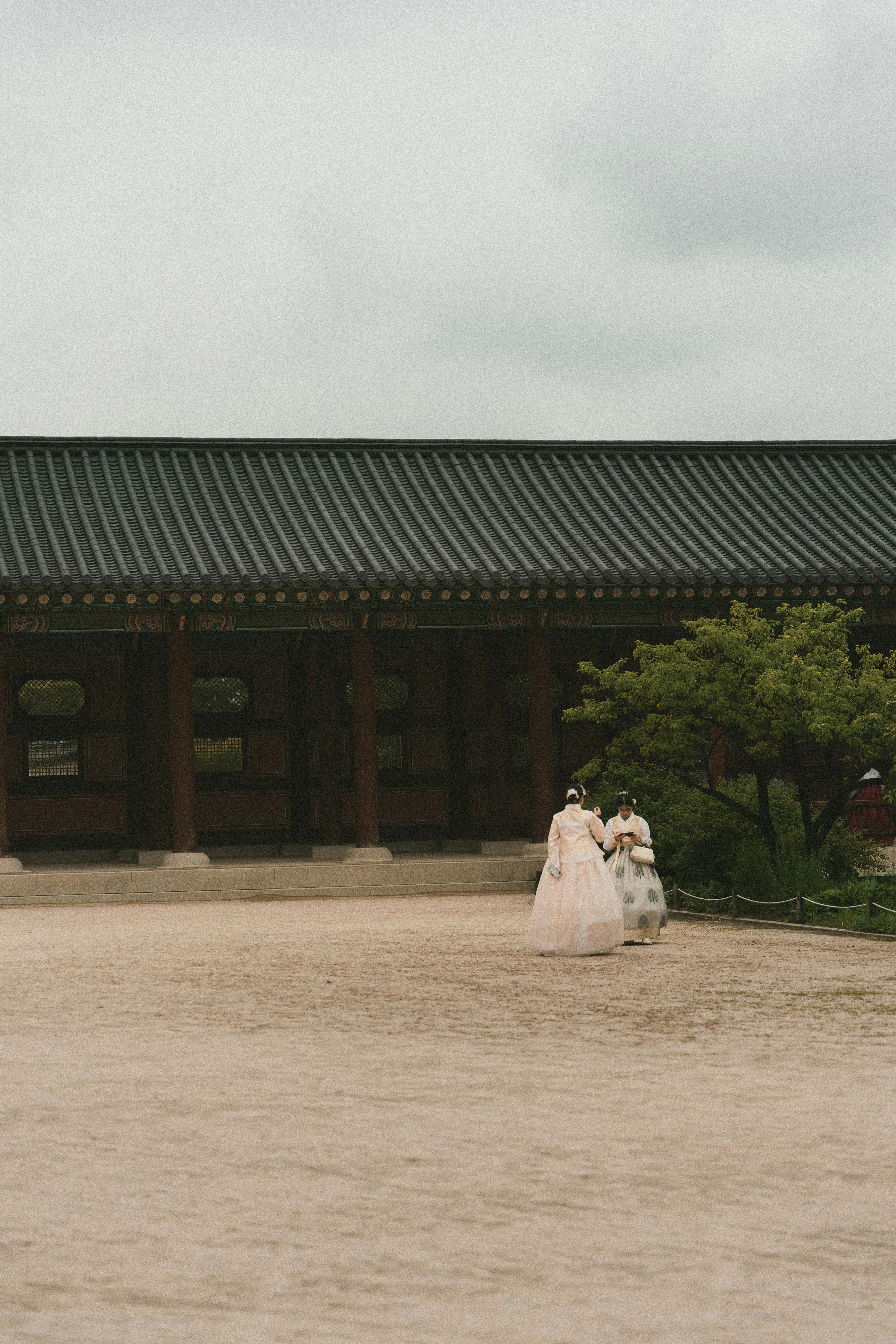 Two women in traditional korean hanbok dresses walk in courtyard.