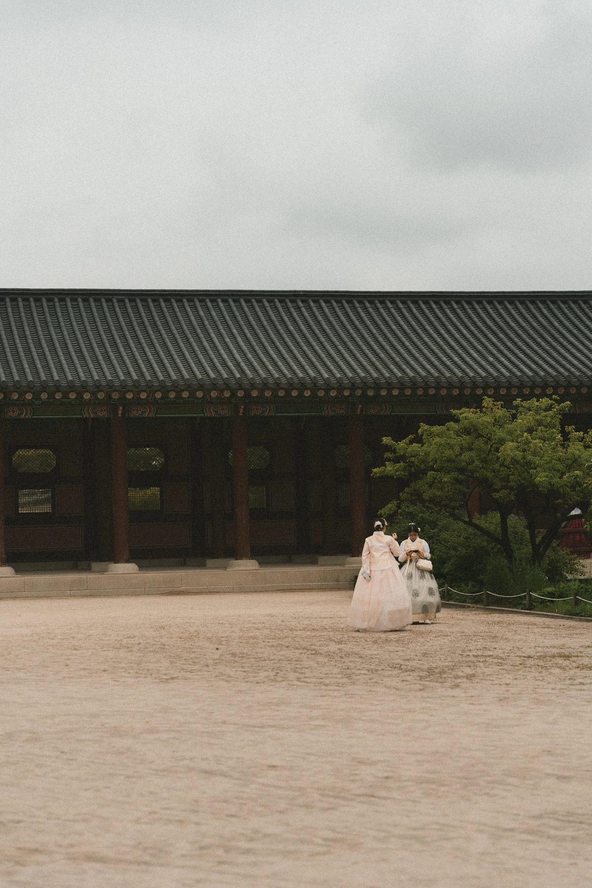 Two visitors in hanbok crossing the courtyard of a Korean palace hall