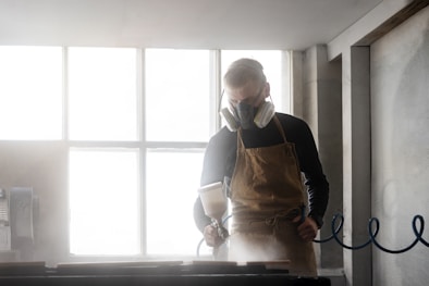 Man wearing respirator and apron working in workshop.