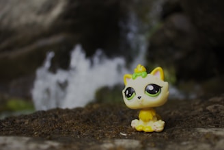 Yellow cat toy sits on dirt with waterfall background.