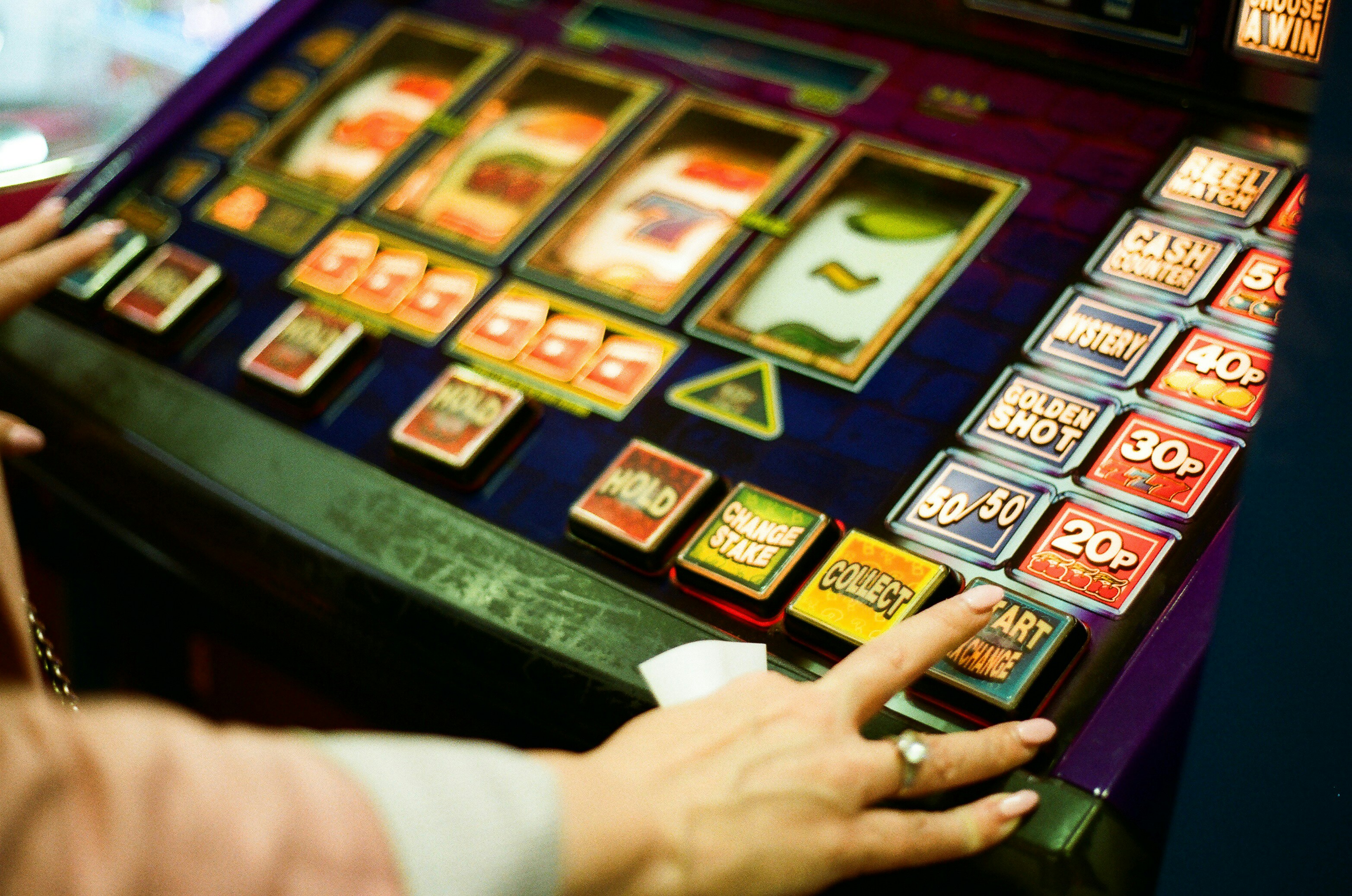 Hands pressing buttons on a colorful slot machine.