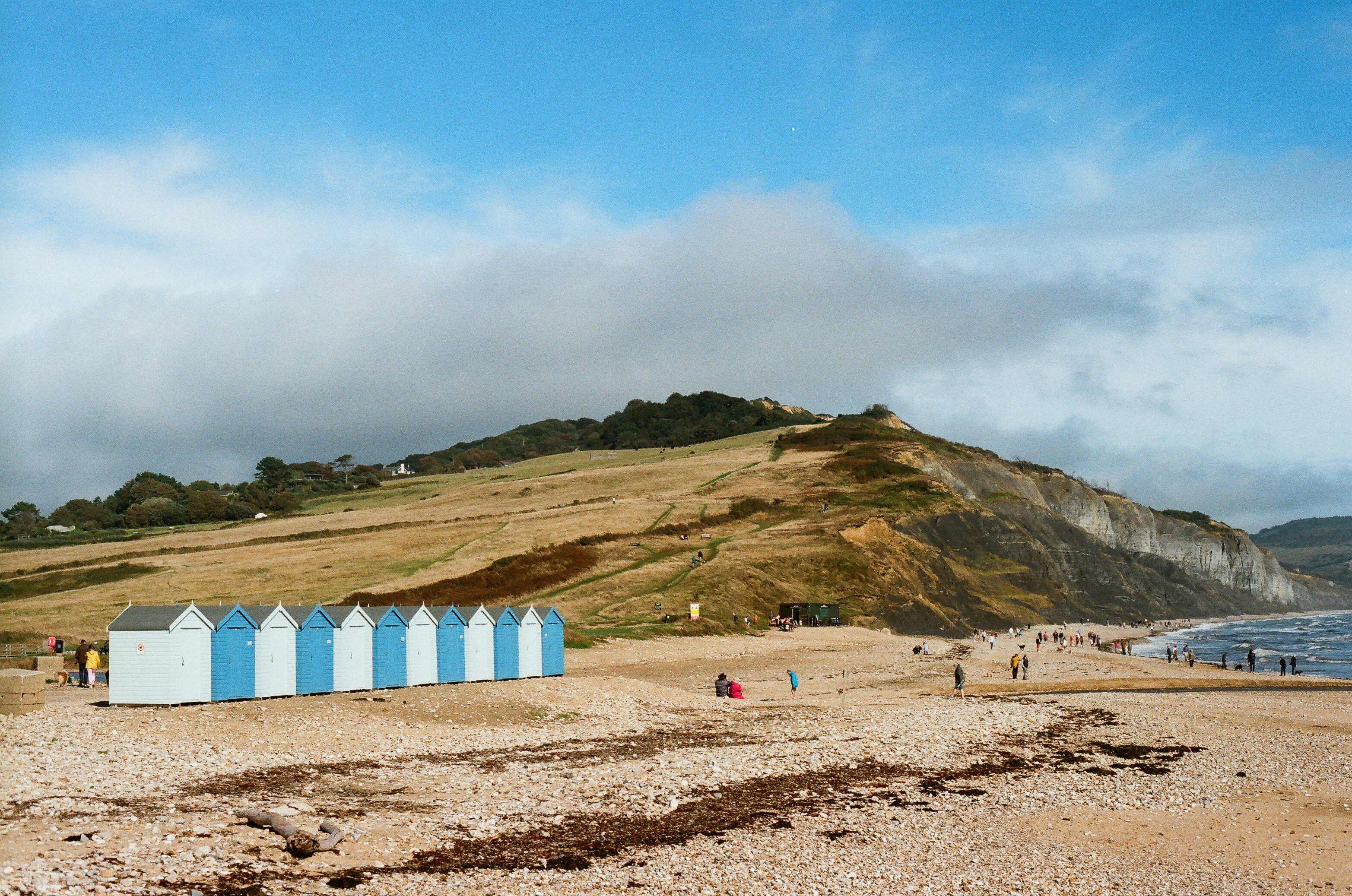 Beach huts line a sandy shore with cliffs and ocean.