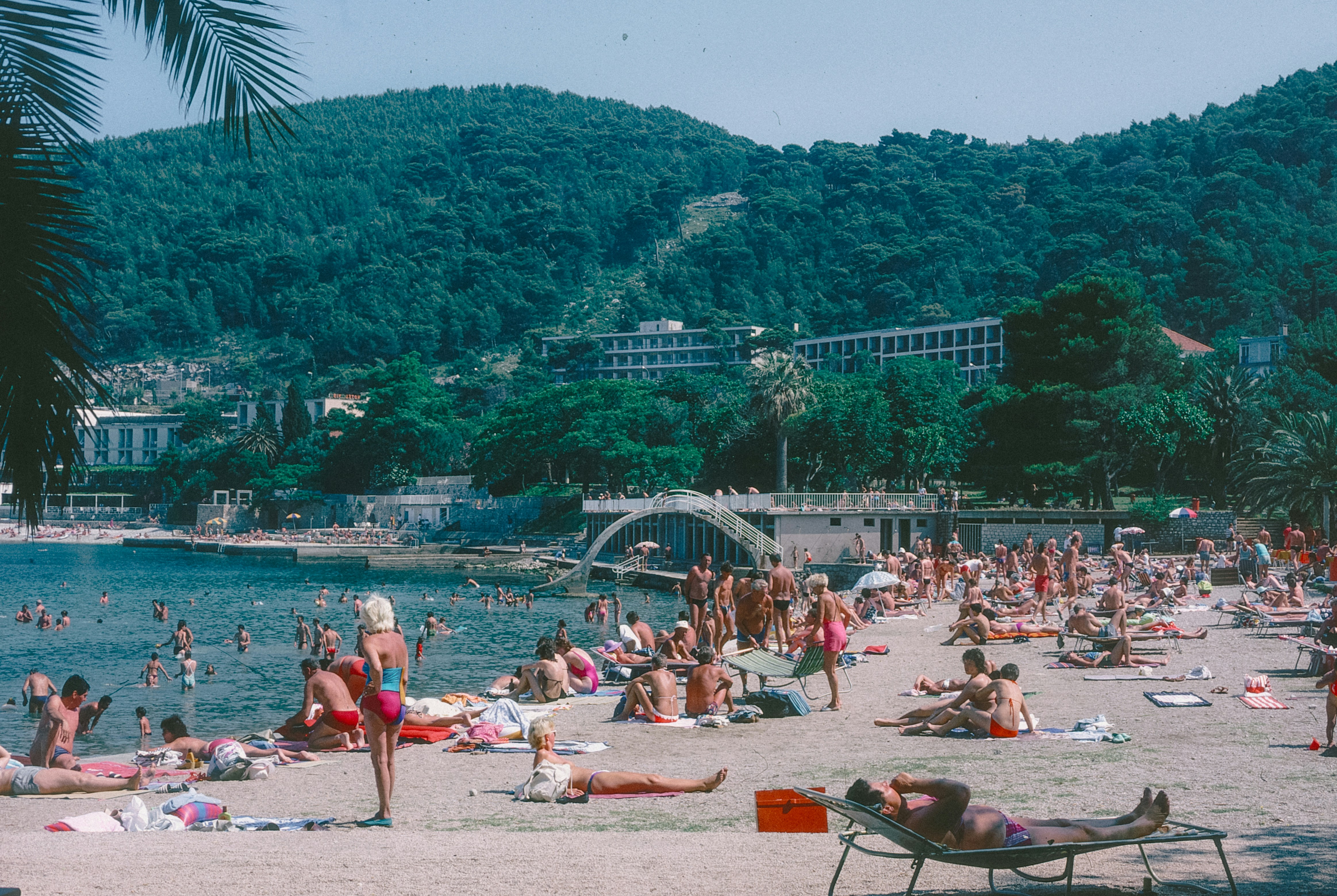 Crowded beach with people sunbathing and swimming by the sea.