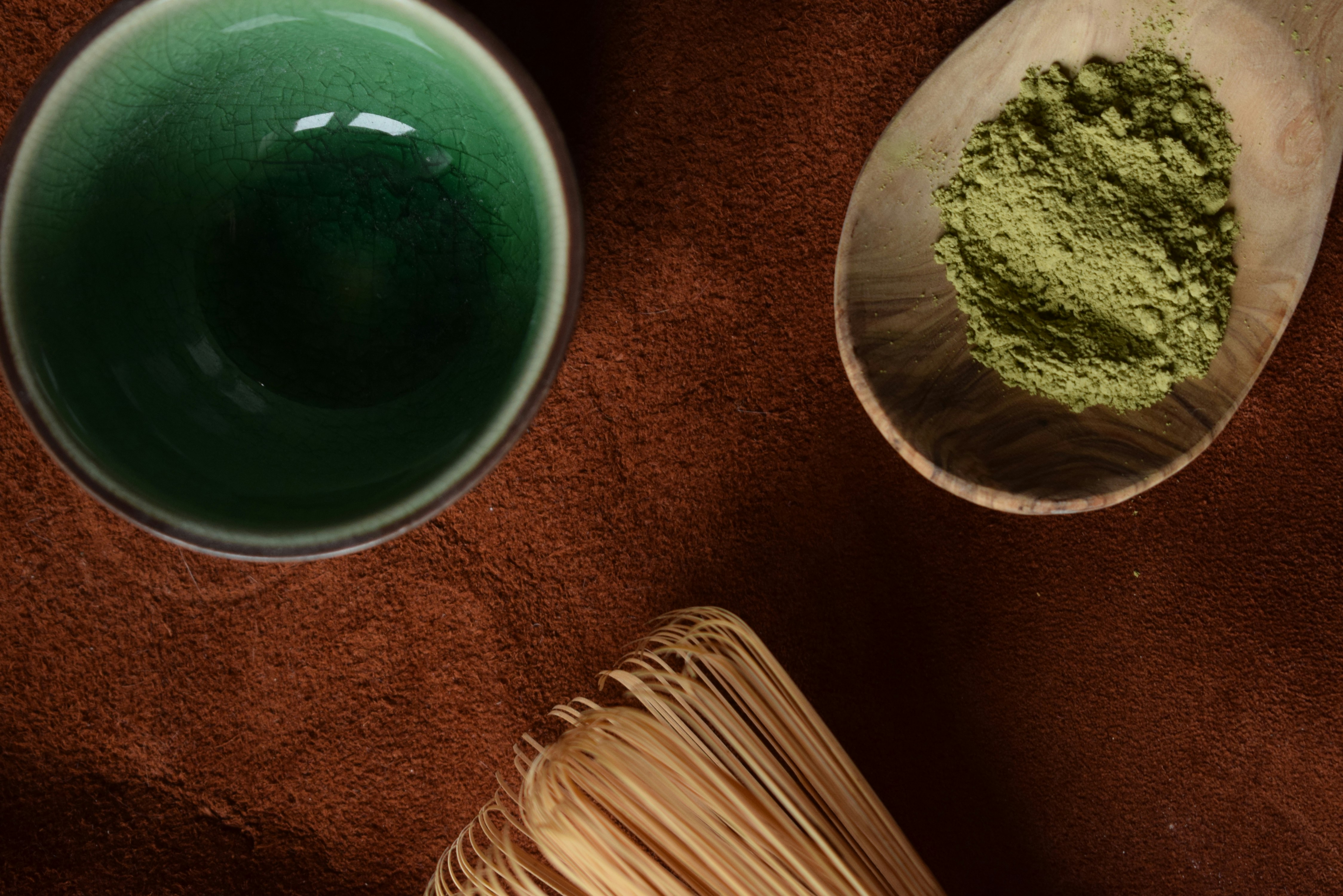 Matcha powder in a wooden spoon with whisk and bowl