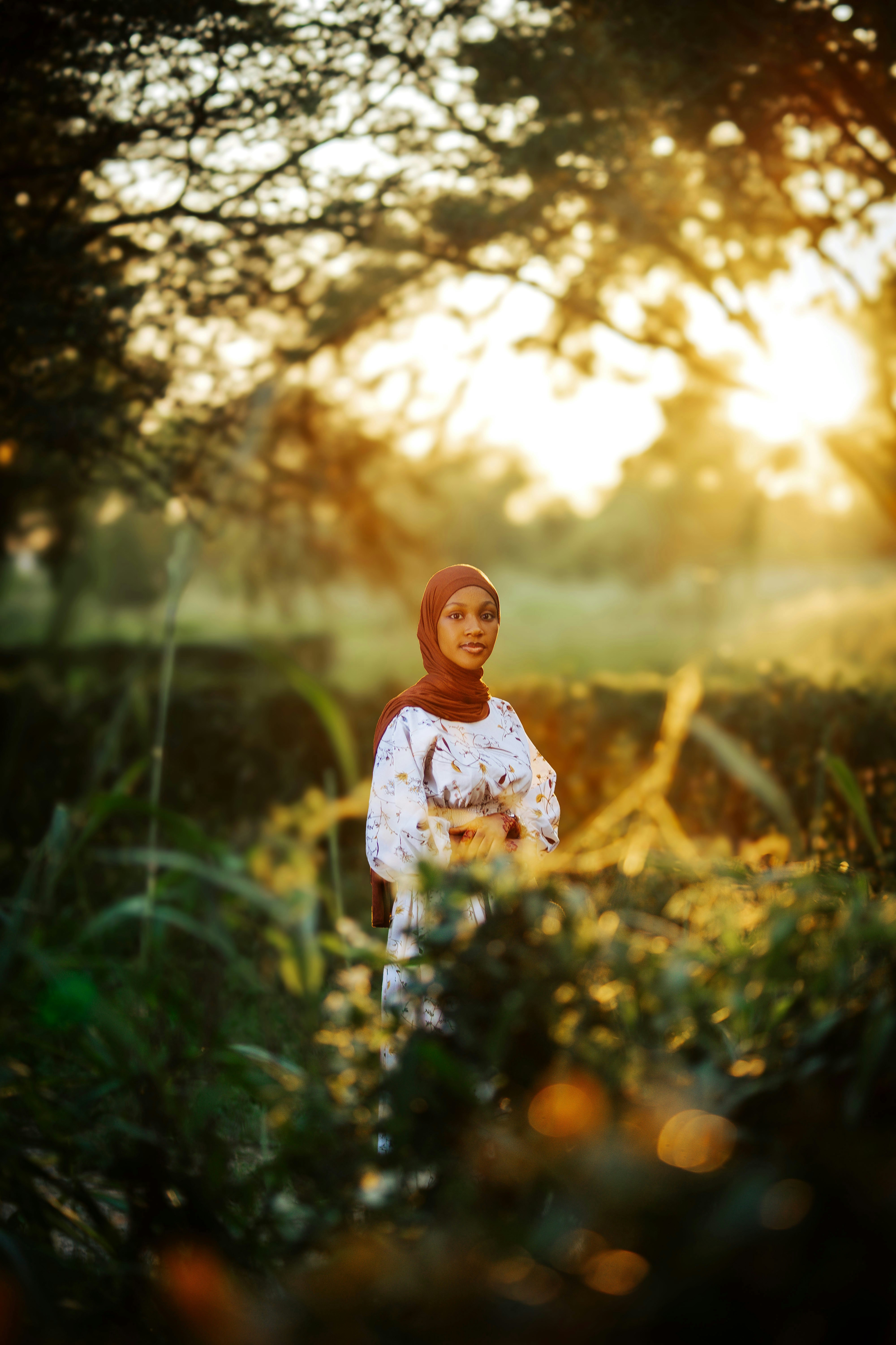 Wanita berjilbab berdiri di taman yang diterangi sinar matahari