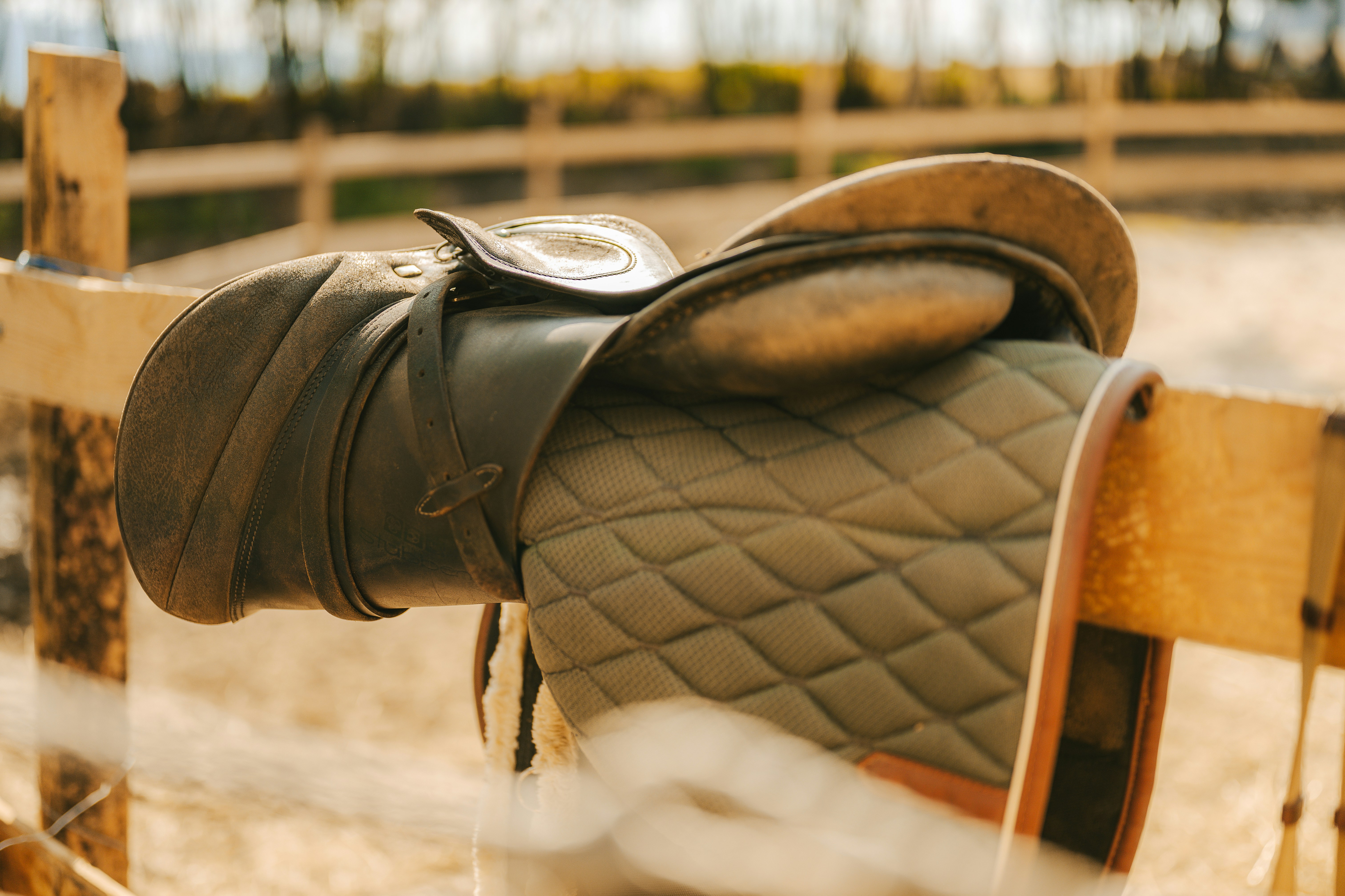 A horse saddle rests on a wooden fence.